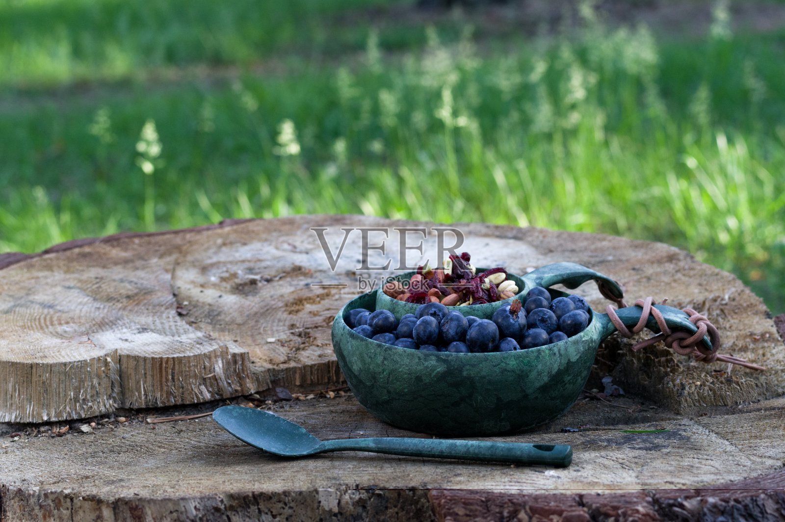 蓝莓和干果放在一个碗里，背景是绿色的草地。在公园里收集浆果和坚果。照片摄影图片