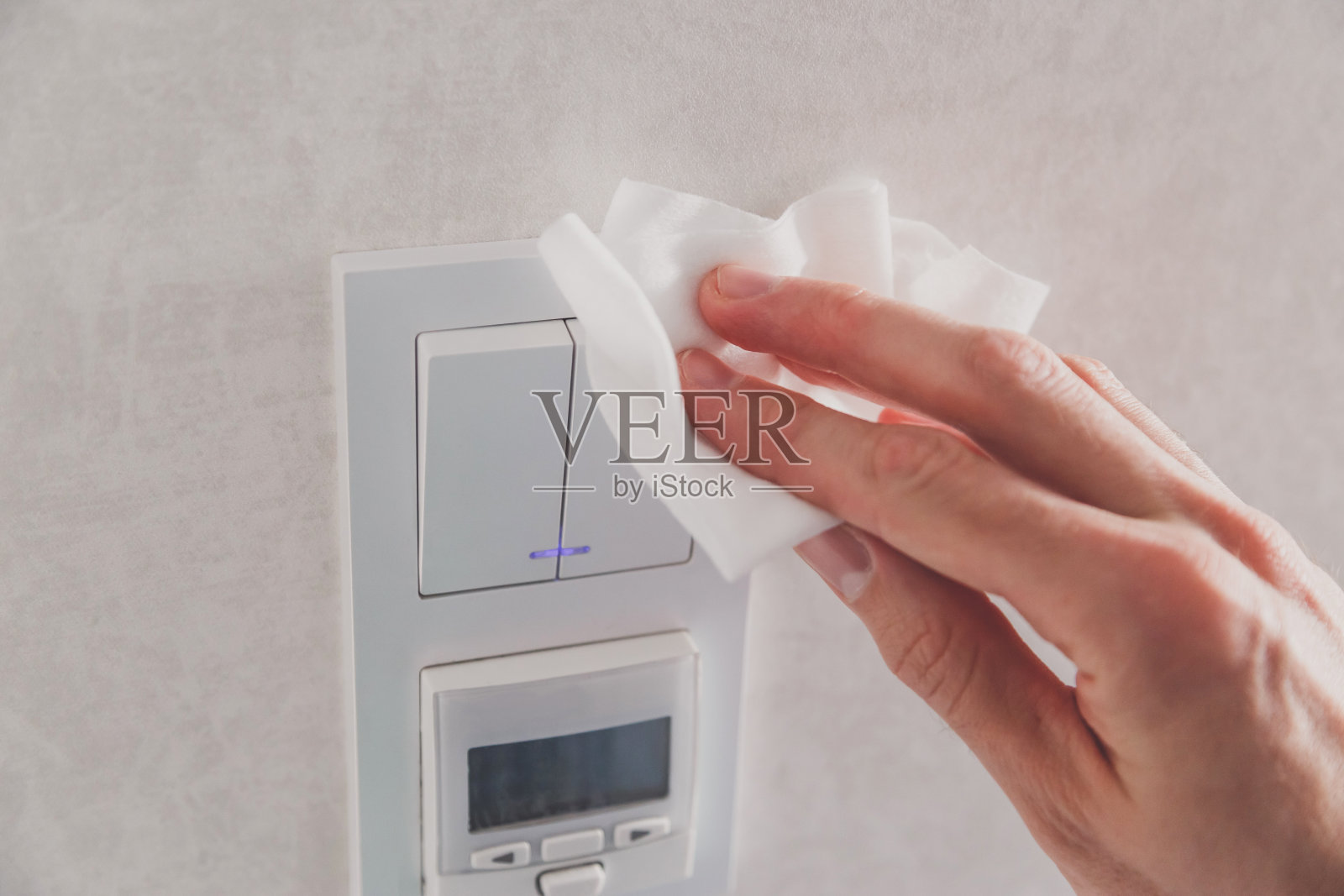 预防感染和病毒，清洁家中厨房的电灯开关时用白色消毒剂擦拭。冠状病毒COVID-19。照片摄影图片