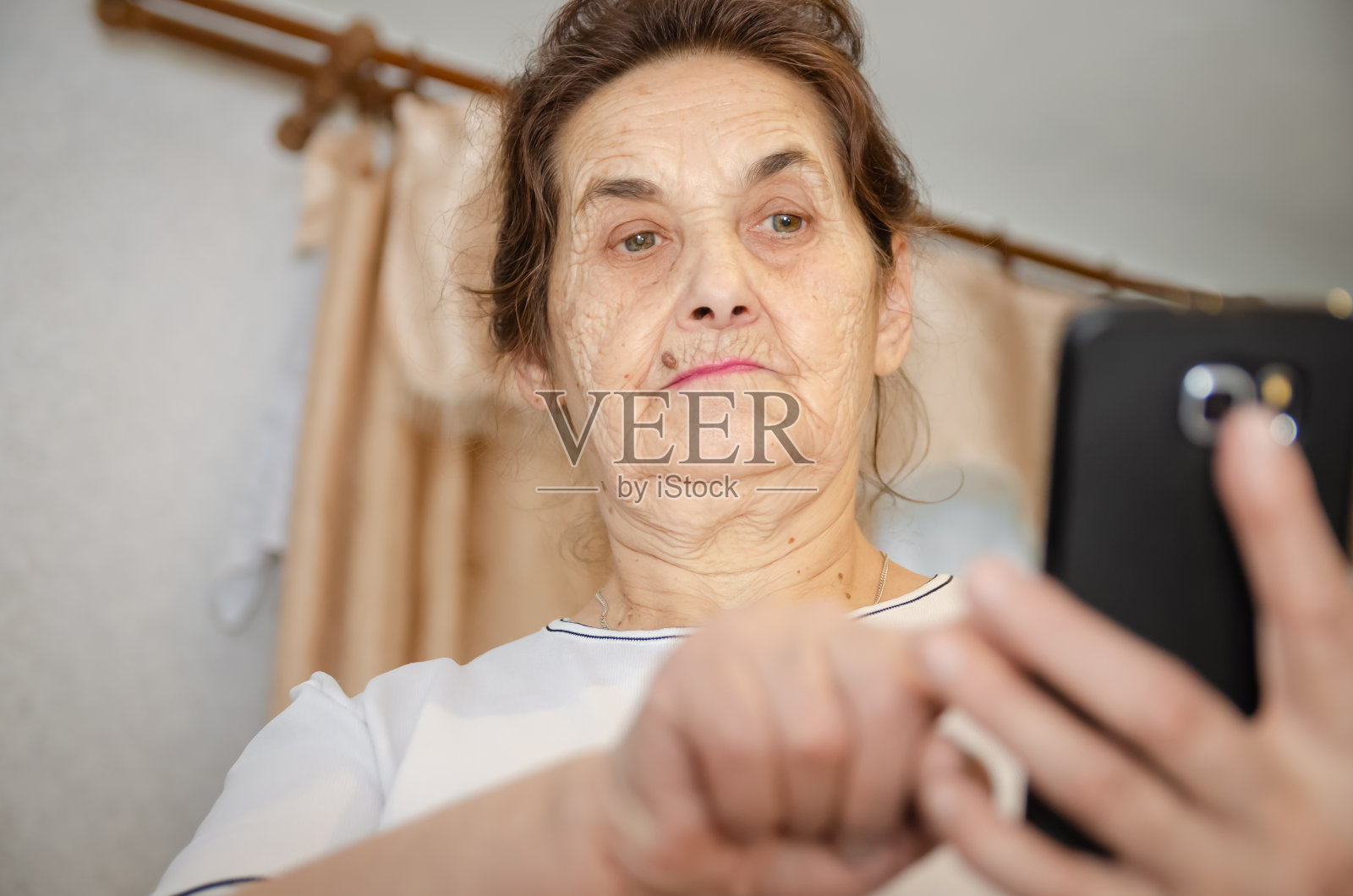 一位黑头发的老妇人拿着一部黑色的手机放在面前，看着它，用手指轻敲着屏幕照片摄影图片