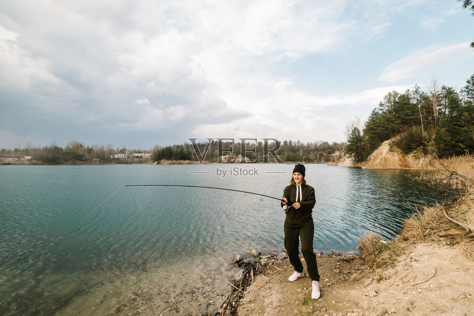 渔夫拿着钓竿，在河岸上旋转卷轴。捕狗鱼、鲈鱼、鲤鱼。在周末钓鱼的时候，一个女人在拉钓竿钓鱼。女孩钓鱼从海滩湖或池塘与文本空间。照片摄影图片