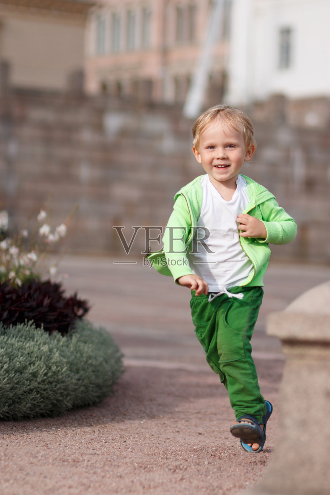 在芬兰的赫尔辛基，一个金发碧眼的孩子穿着绿色的衣服在参议院广场上快乐地奔跑。照片摄影图片