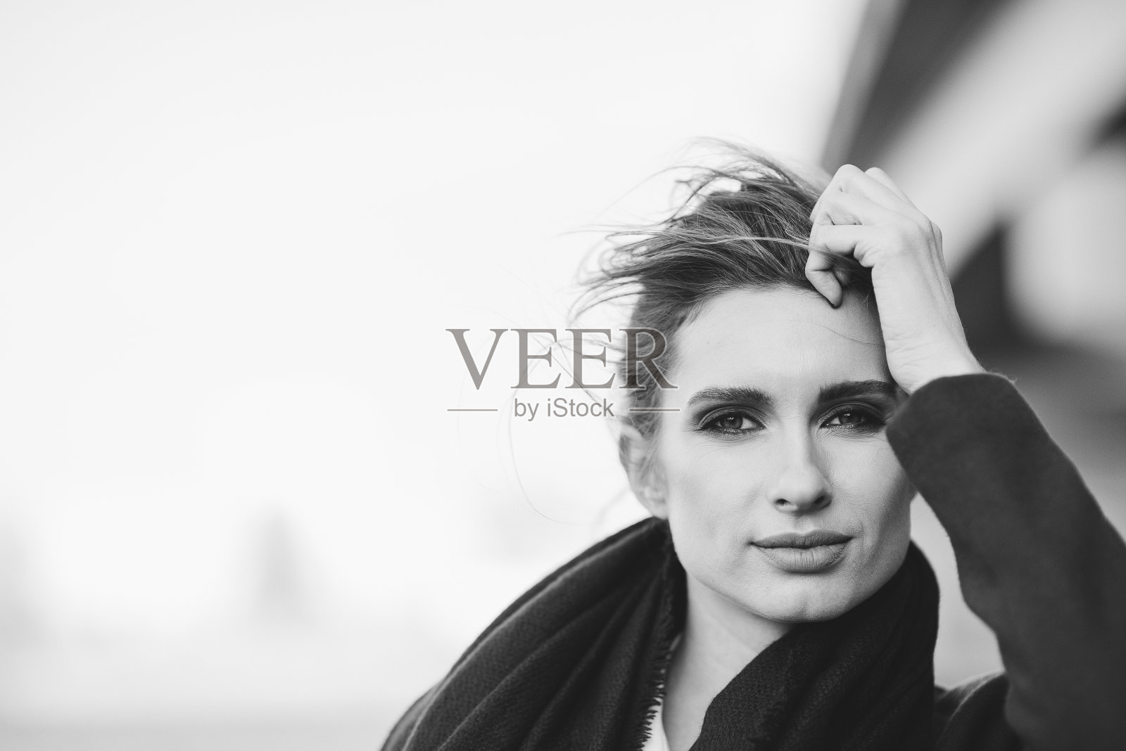 一个美丽孤独的女人，穿着大衣，围着围巾，头发在寒冷灰暗的日子里在桥下随风飘动。孤独的概念。黑白艺术照片。软选择聚焦。照片摄影图片