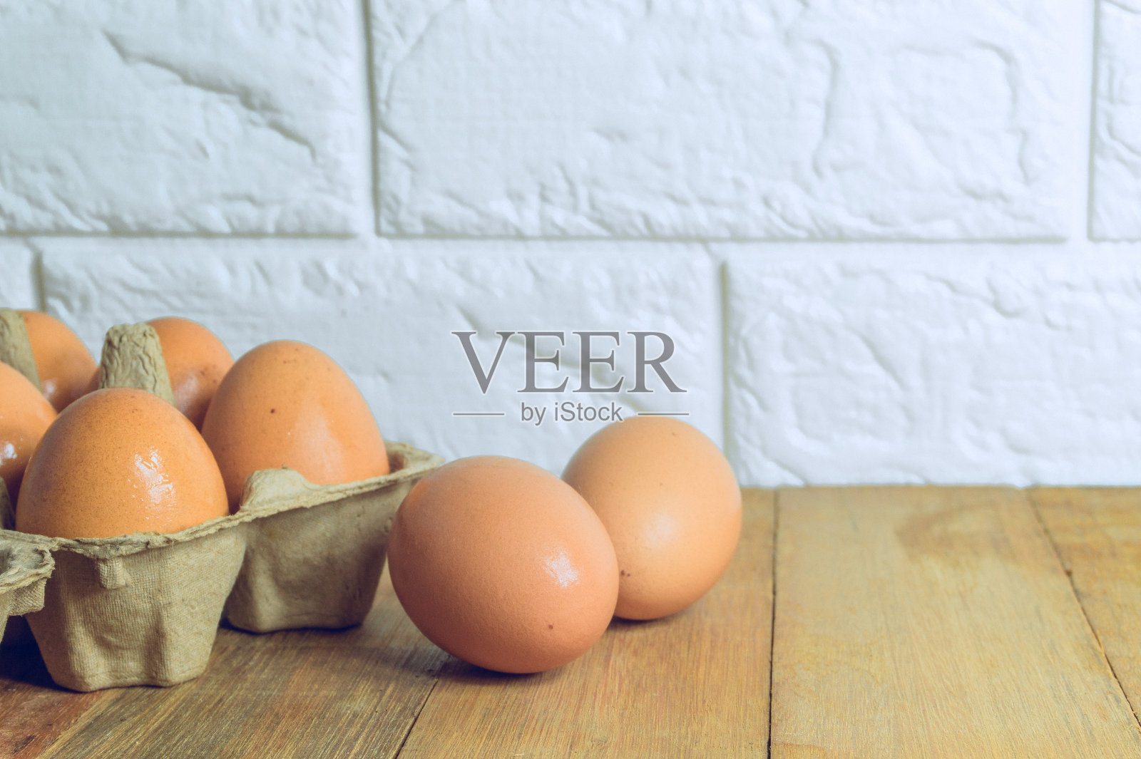 鸡蛋放在纸盘里，鸡蛋放在厨房的木桌上，背景是砖砌的照片摄影图片