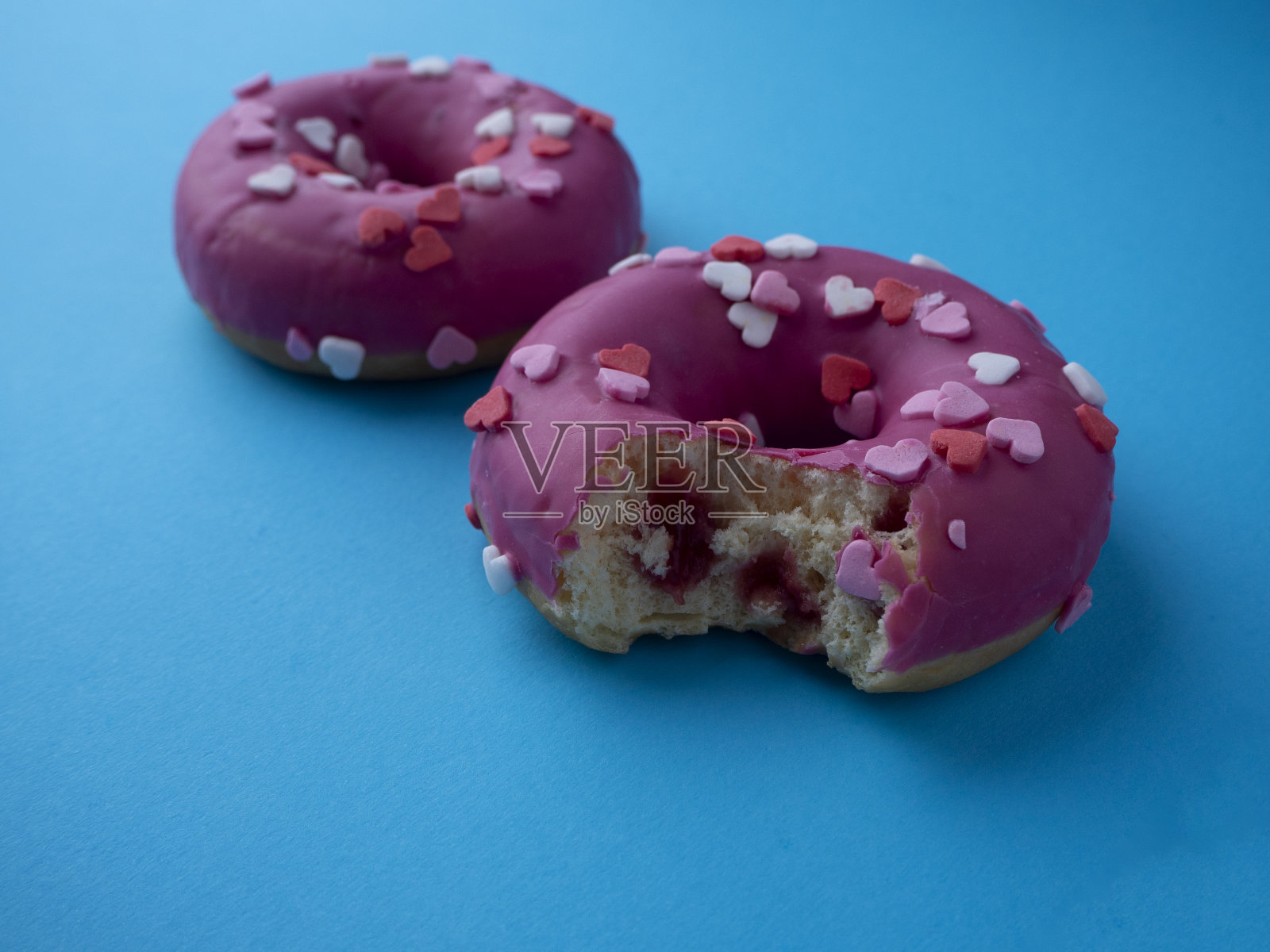 蓝底浆果馅咬甜甜圈。两个用心形装饰的粉色甜甜圈。照片摄影图片