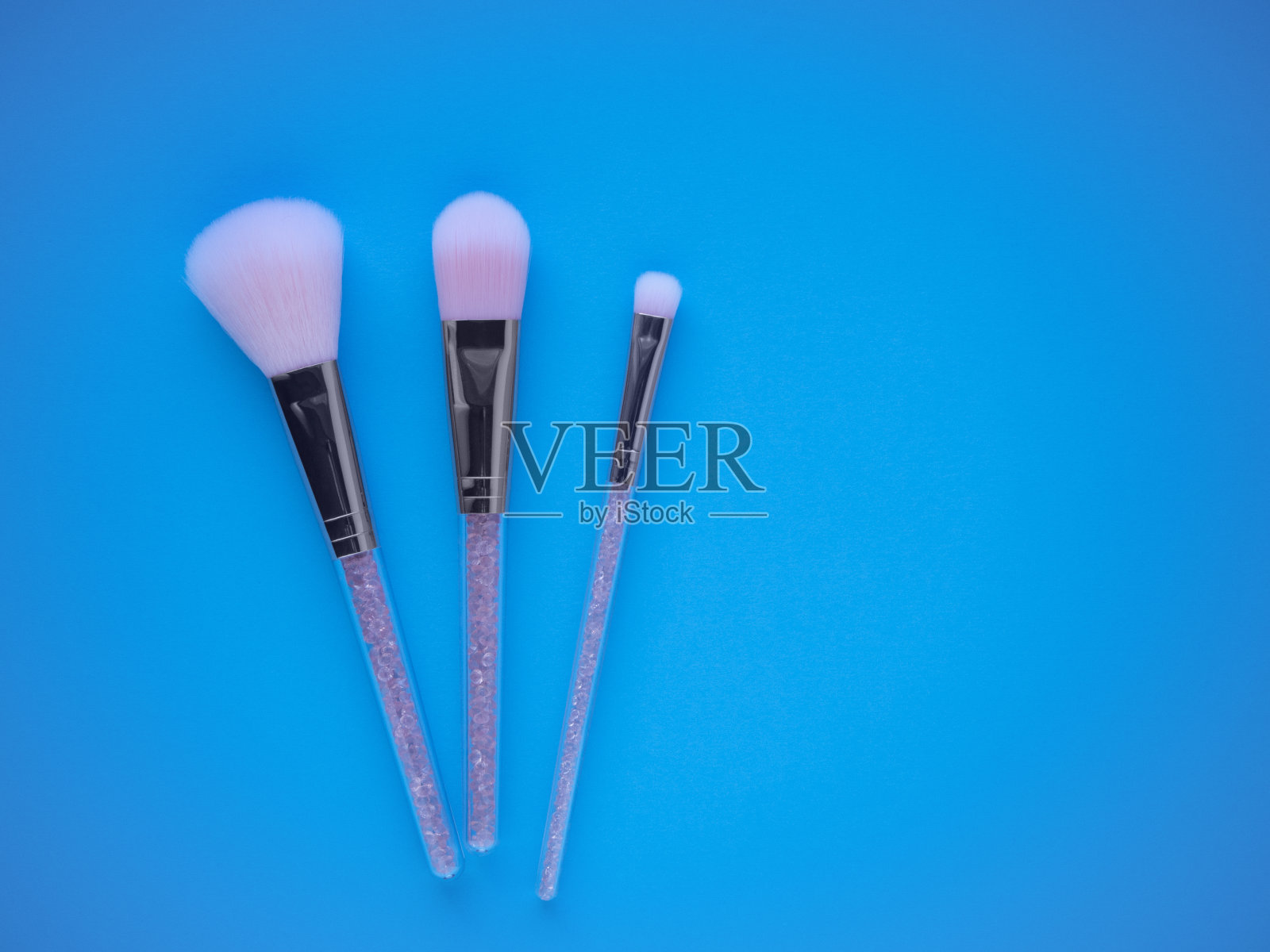 粉色化妆笔刷在蓝色背景顶视图与复制空间。专业化妆用粉刷、腮红刷、眼影刷。照片摄影图片