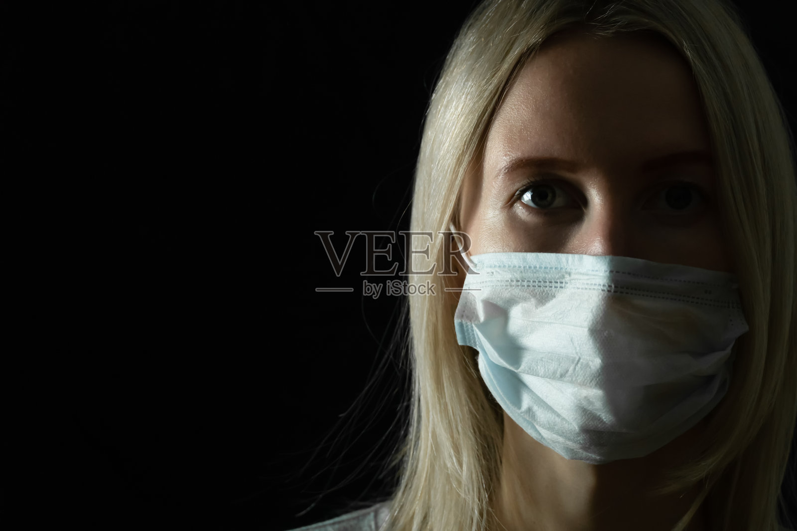 年轻的金发女人戴着医用面具，黑色背景上有拷贝空间照片摄影图片