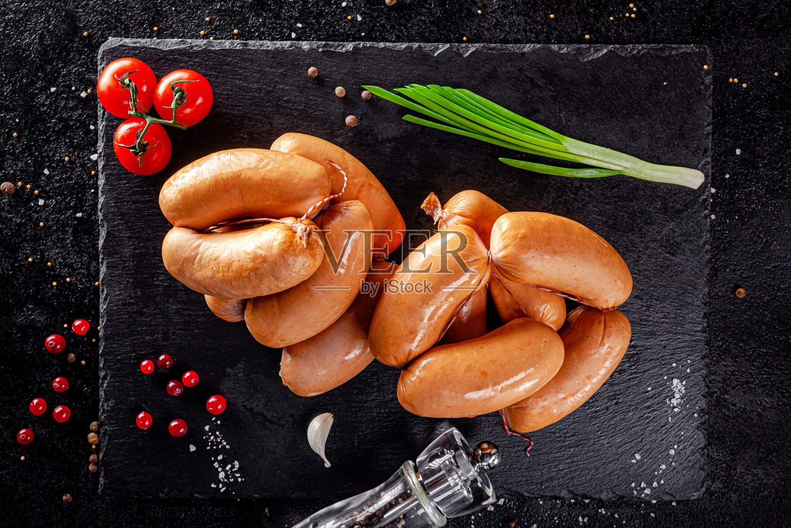 各种各样的香肠和烟熏制品躺在一块黑板子上，有香肠、香肠、排骨、面包卷。顶视图,开销。平躺照片摄影图片