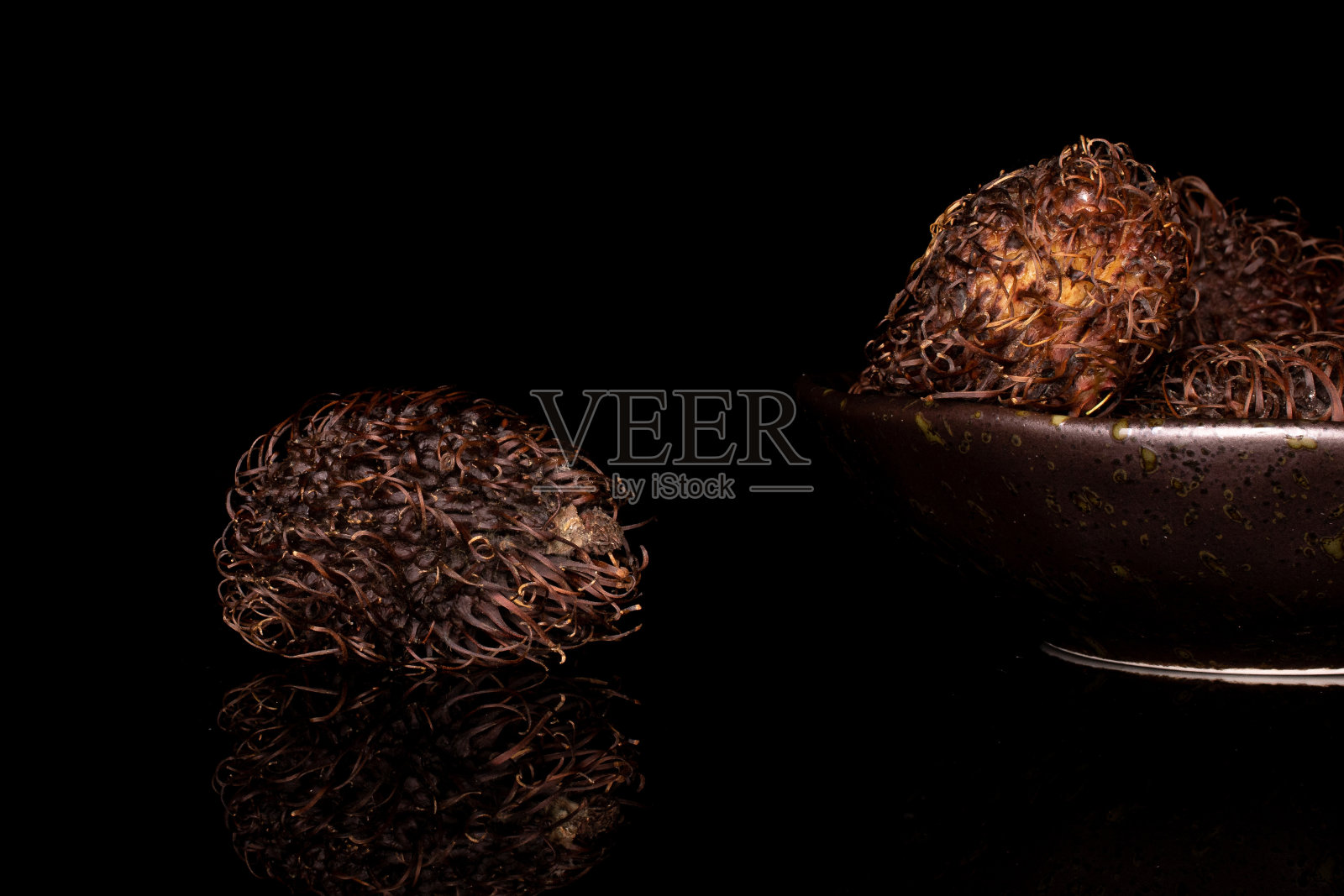 老棕色红毛丹孤立在黑色玻璃上照片摄影图片