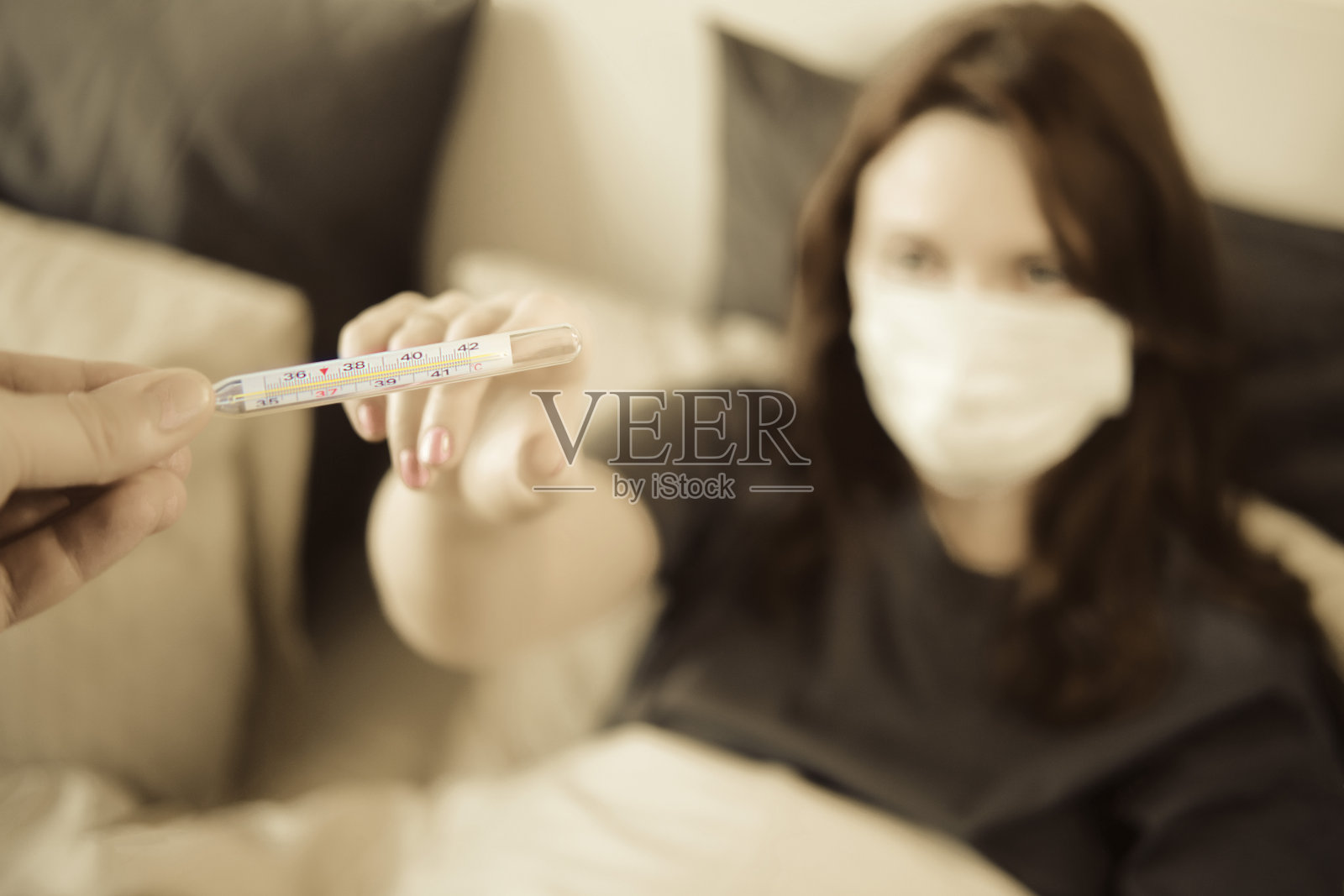 一名患有冠状病毒流感的红头发妇女戴着医用口罩，从医生那里拿着体温计照片摄影图片