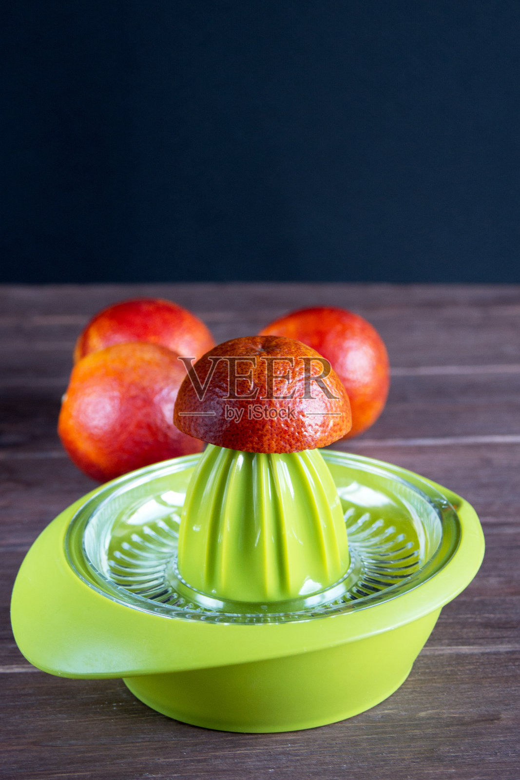 桌上的绿色手动榨汁机是用来榨取红色西西里橙汁的。照片摄影图片