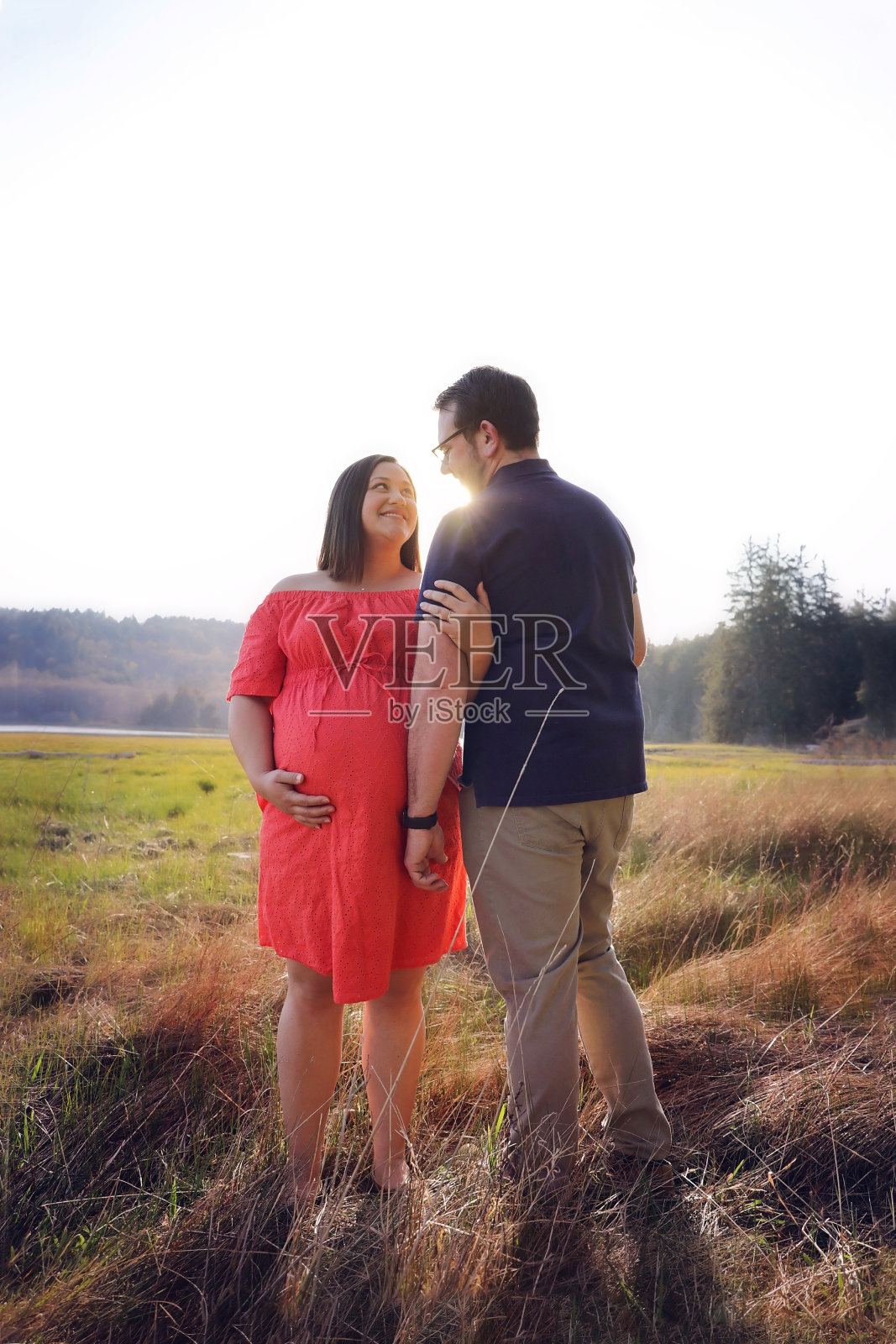 丈夫和怀孕的妻子在外面的田野里微笑着父亲，身后是阳光照片摄影图片