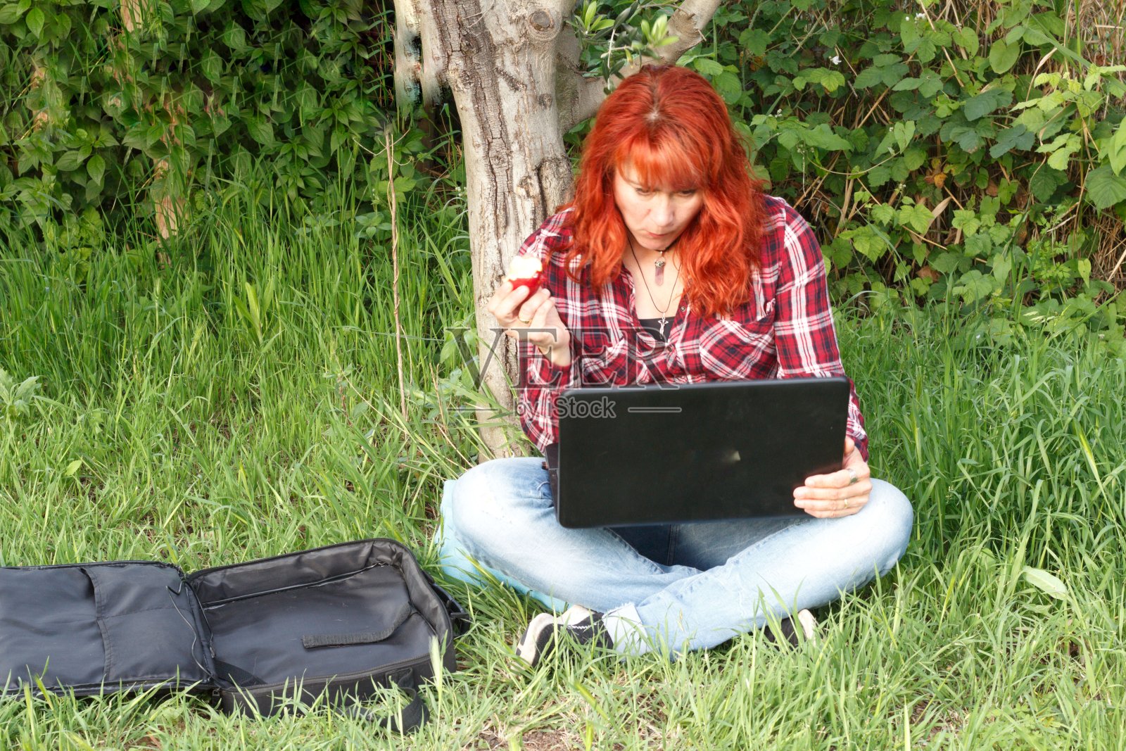 一个白人女人一边在公园里玩电脑一边吃苹果照片摄影图片