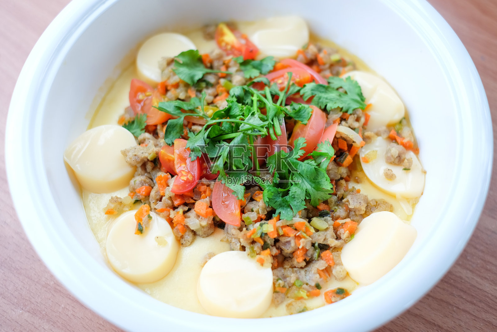 荷包蛋配上猪肉、豆腐、西红柿和蔬菜(蒸蛋)，放在白色的碗里，放在棕色的桌子上——这是家常食物的概念。照片摄影图片