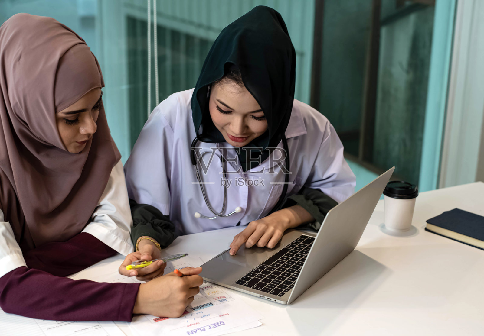 两位女医生使用笔记本电脑咨询病人，在医院工作，繁忙的时间照片摄影图片