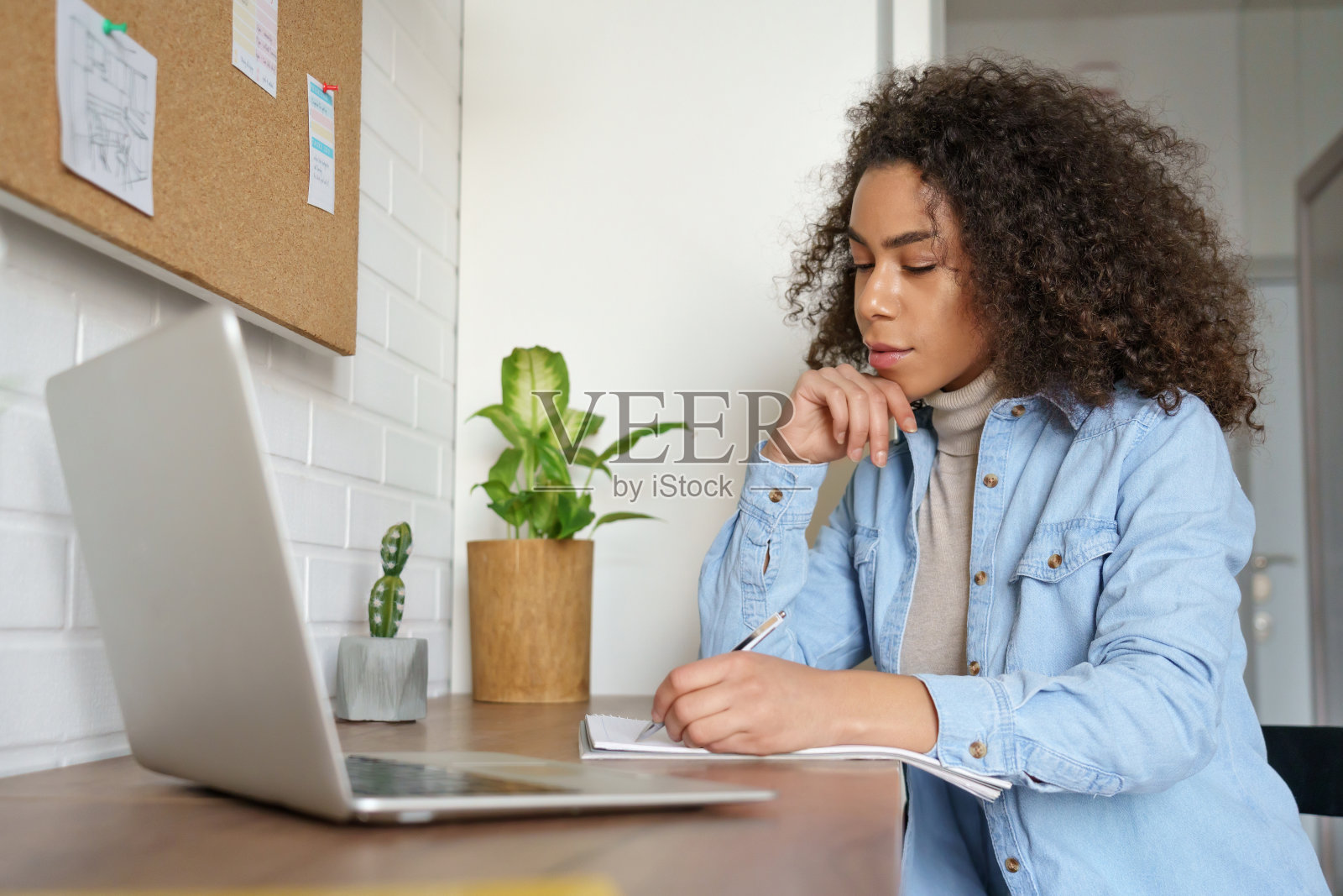 在家学习的非洲裔女学生观看教育培训网络研讨会，通过电脑进行视频会议，并通过导师进行在线学习并做笔记照片摄影图片
