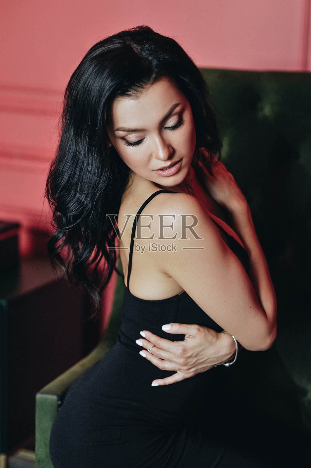 美丽的女孩与亚洲人的外表。肩带上的黑色试衣。长长的黑发。红色的墙。赤脚。绿色的椅子上。黄色的花朵。性感和聪明的女人。肖像。照片摄影图片