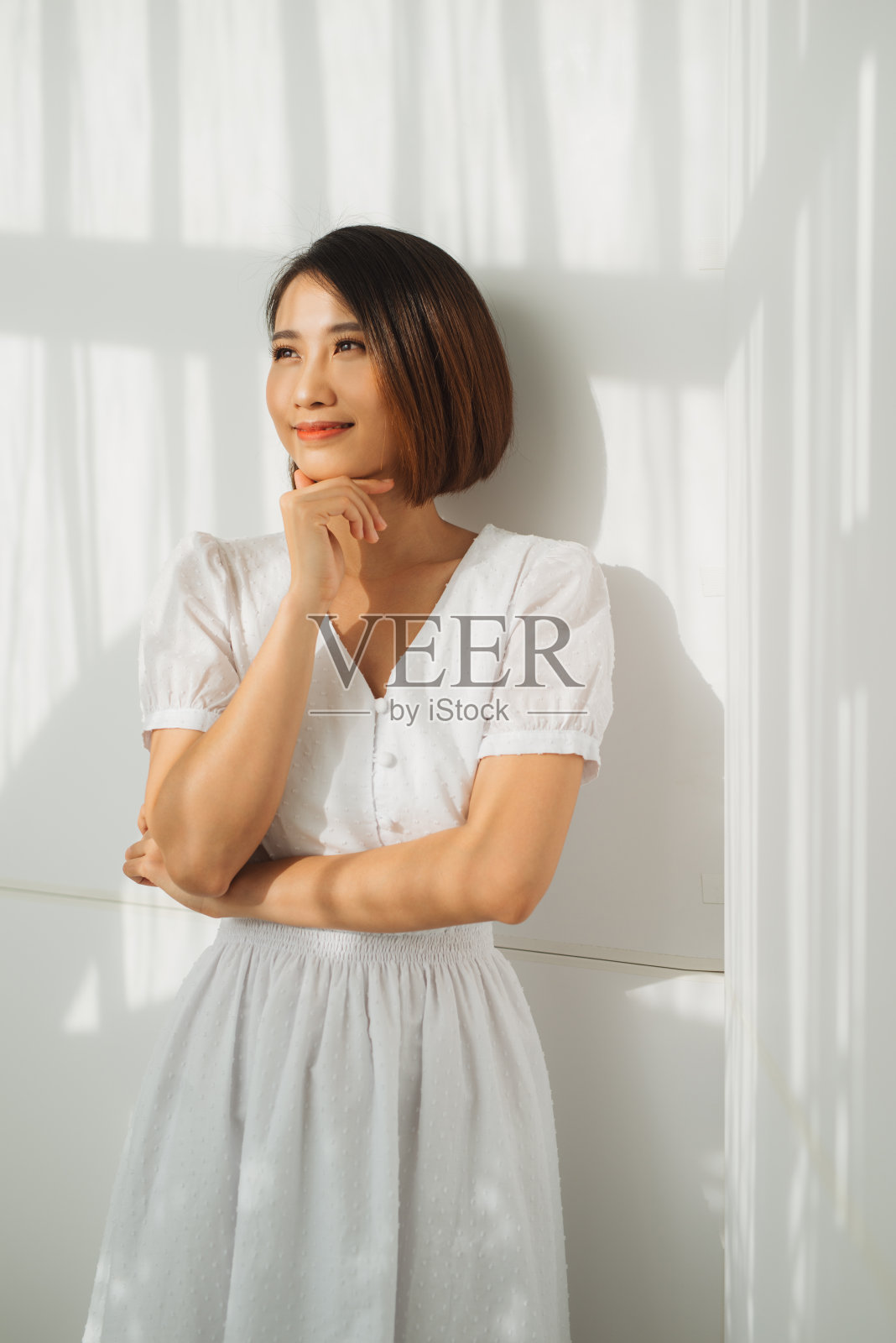 美丽优雅的女子靠墙站着，阳光是美丽的落下照片摄影图片