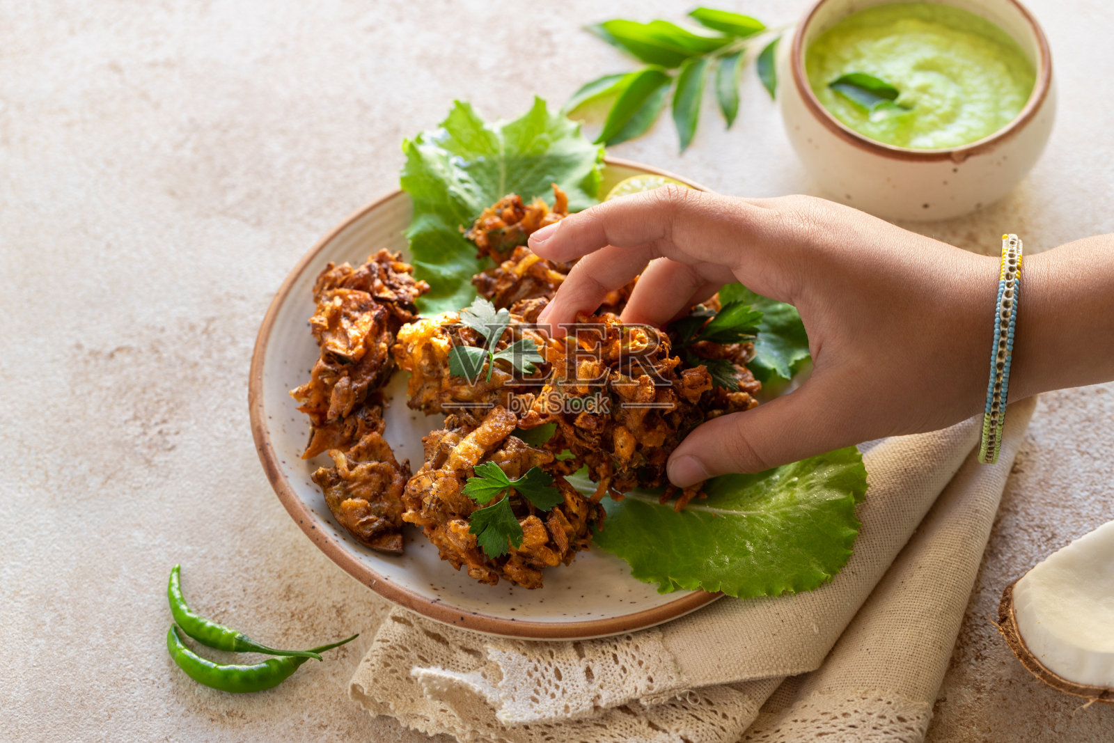 印度菜印度菜。椰汁辣酱烤Pakora咖喱叶。年轻的印度妇女或孩子的手从盘子里拿起炸蔬菜。正宗的亚洲素食。手游食品照片摄影图片