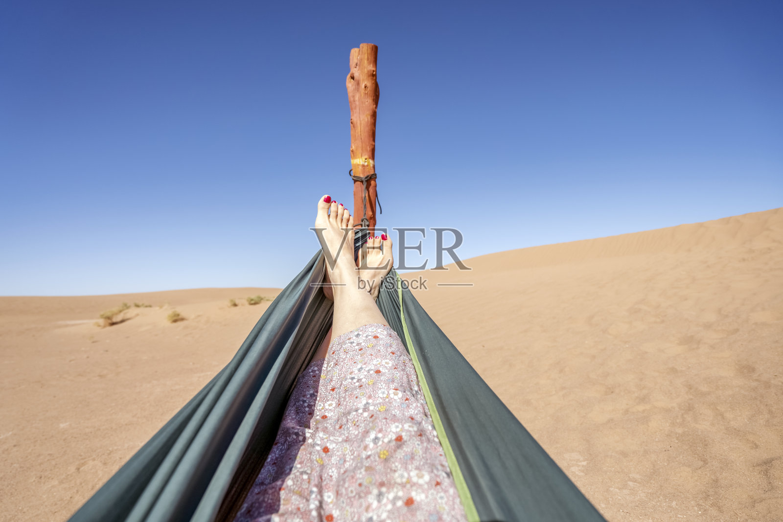 年轻女子在绿色吊床上放松，在摩洛哥撒哈拉沙漠的沙丘上看风景。照片摄影图片