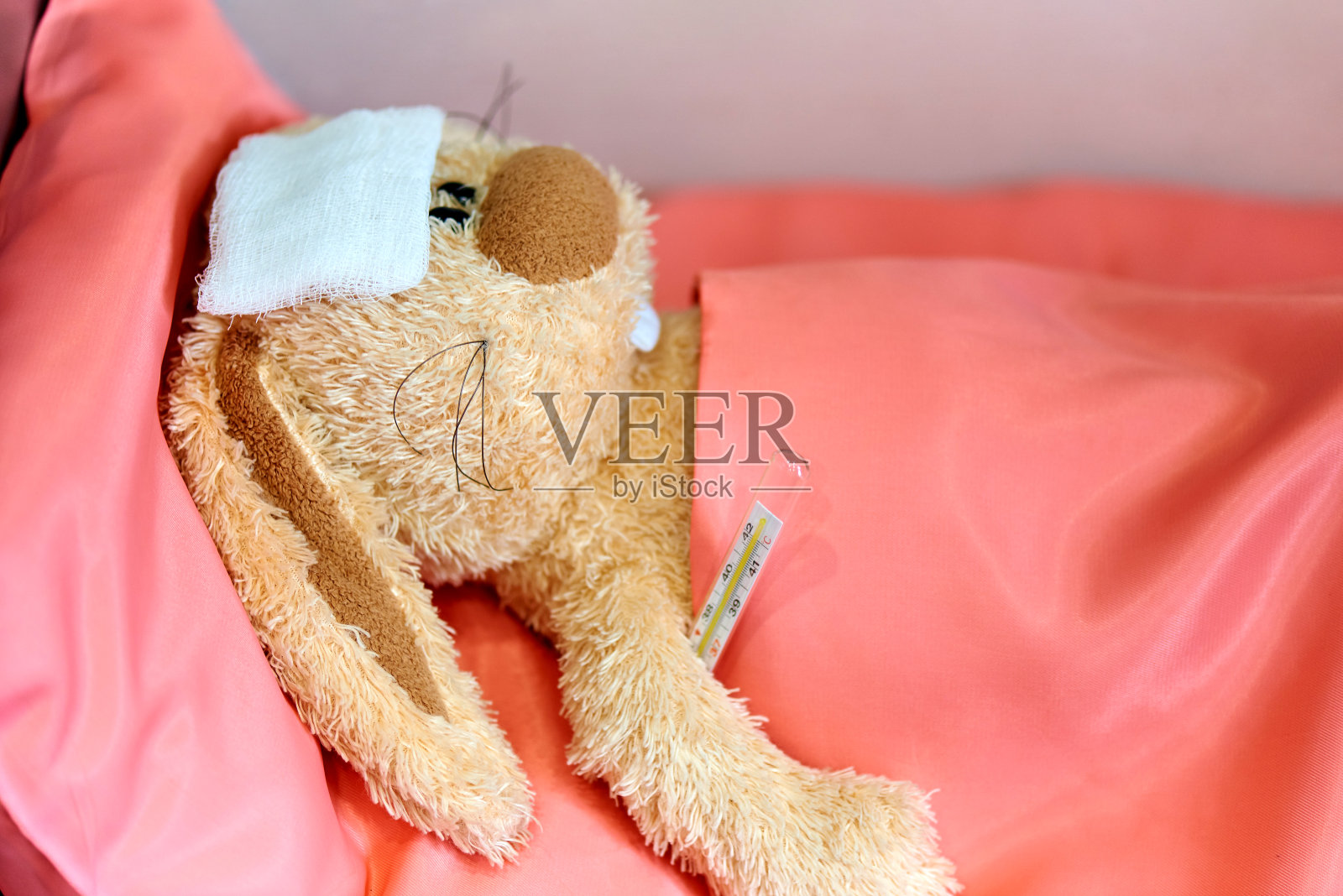 一只生病的毛绒兔子在床上测量温度。照片摄影图片