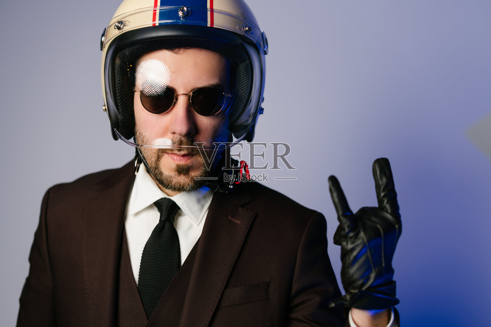 摩托车手穿着西装，戴着头盔，做着摇滚喇叭手势照片摄影图片