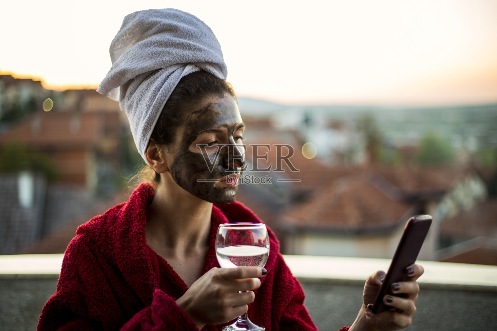 美丽的年轻女子，戴着黑色面膜。喝一杯水，使用电话照片摄影图片