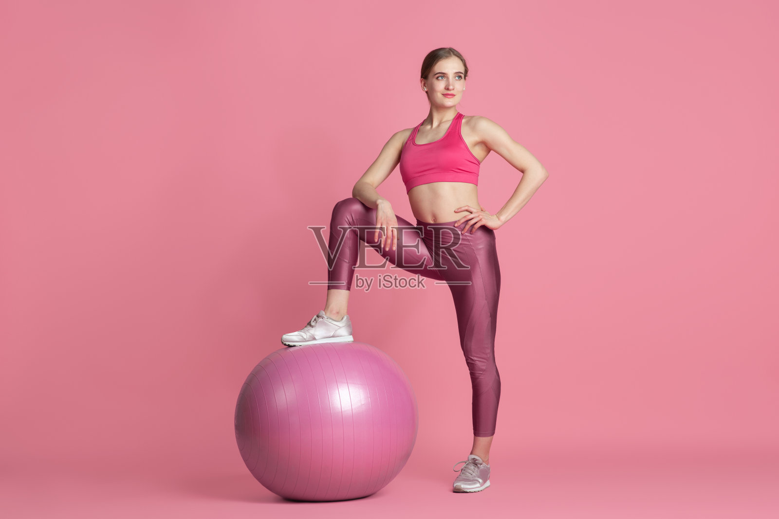 美丽的年轻女运动员练习在粉红色的工作室背景，单色肖像照片摄影图片