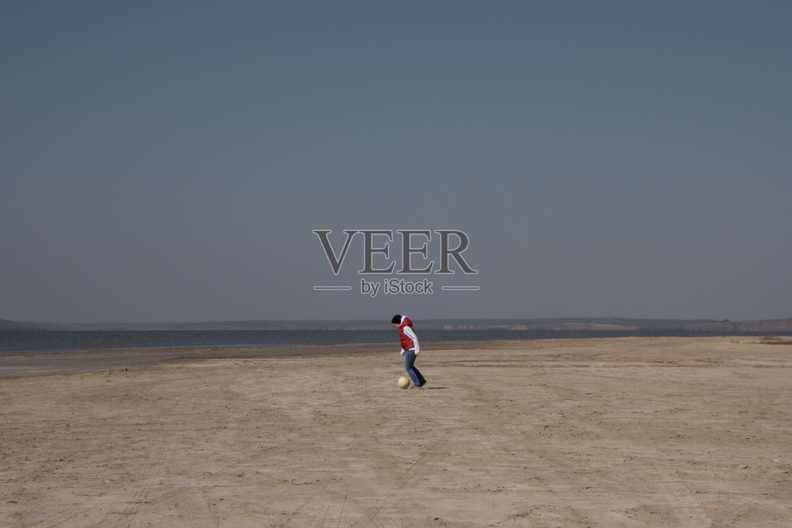 10岁男孩在空旷的沙滩上独自踢足球照片摄影图片