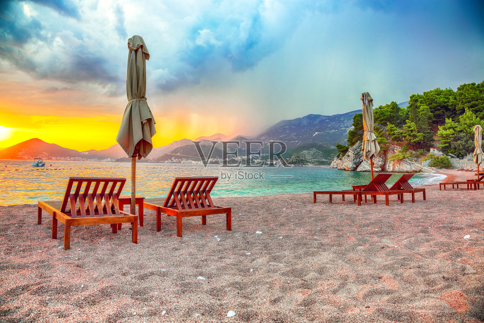 在靠近Budva的Sveti Stefan的沙滩上戏剧性的日落与躺椅和雨伞照片摄影图片