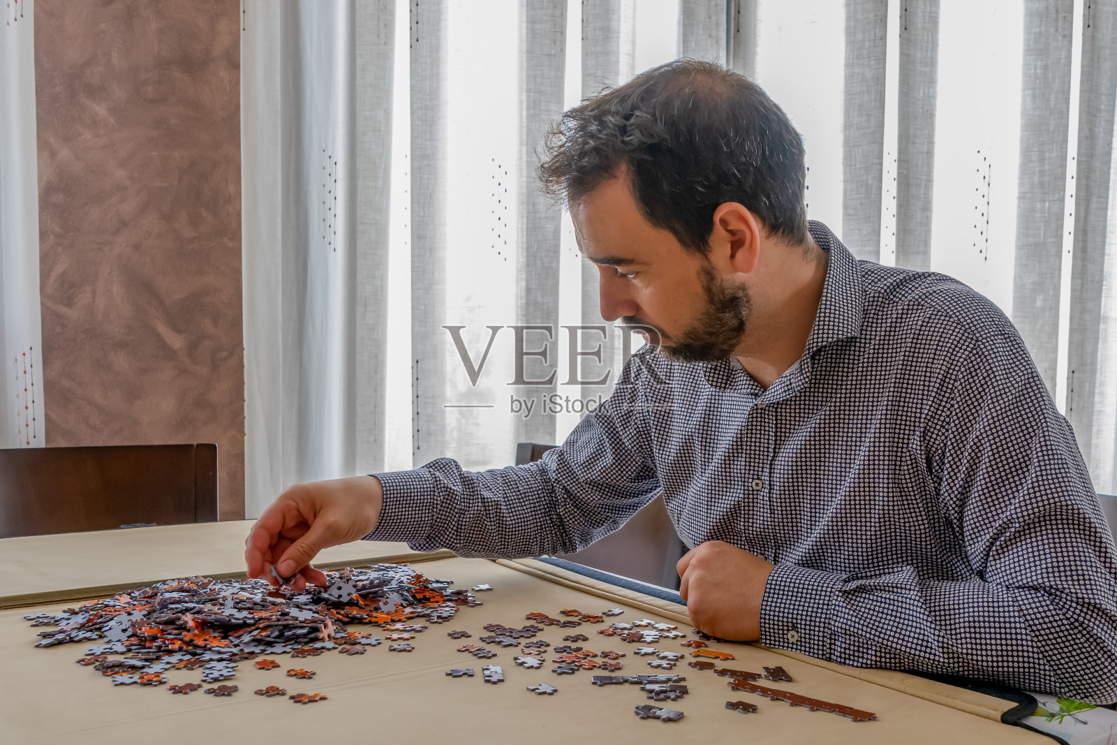 穿着黑白衬衫的大胡子男人在客厅玩拼图游戏照片摄影图片