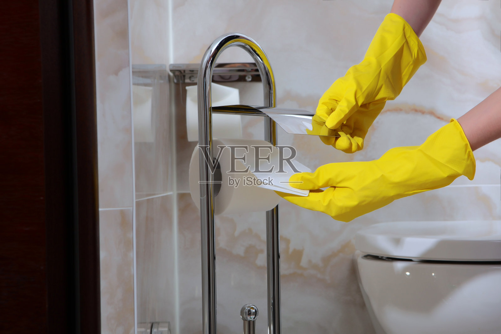 妇女的手在橡胶保护手套擦拭厕纸架。照片没有脸，只有手。浴室的清洁卫生。照片摄影图片