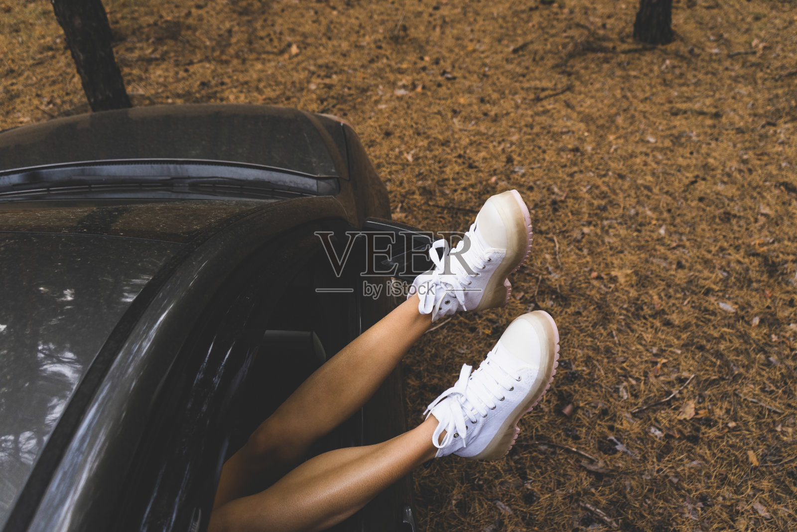 享受，在森林里放松，慵懒周日，旅游，旅游，自由时间，休息，幸福的理念。一个穿着白色靴子的年轻女孩的腿在一辆汽车的车窗上，在一片针叶林的背景下，平躺着。照片摄影图片