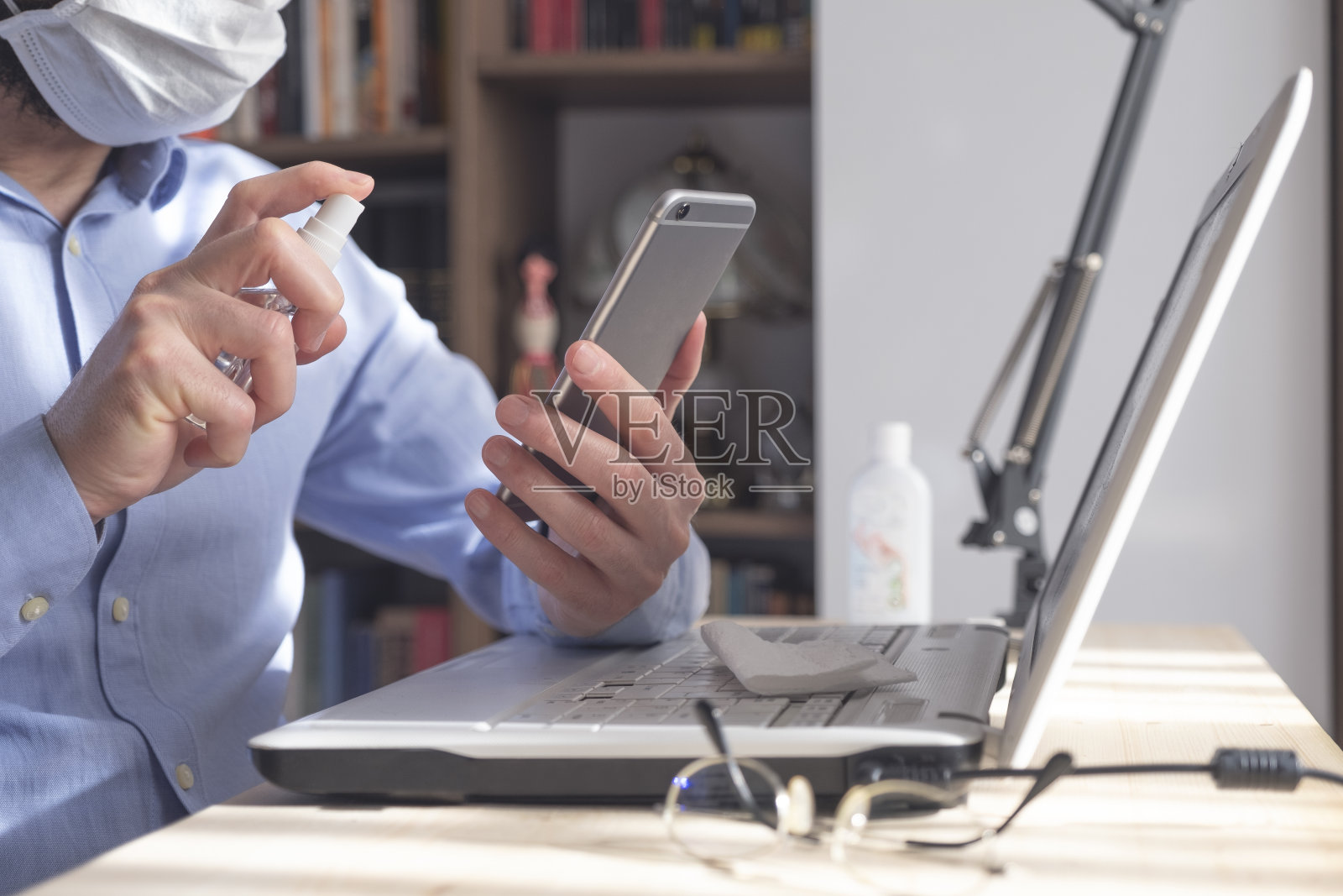小心翼翼的蒙面人给手机消毒照片摄影图片