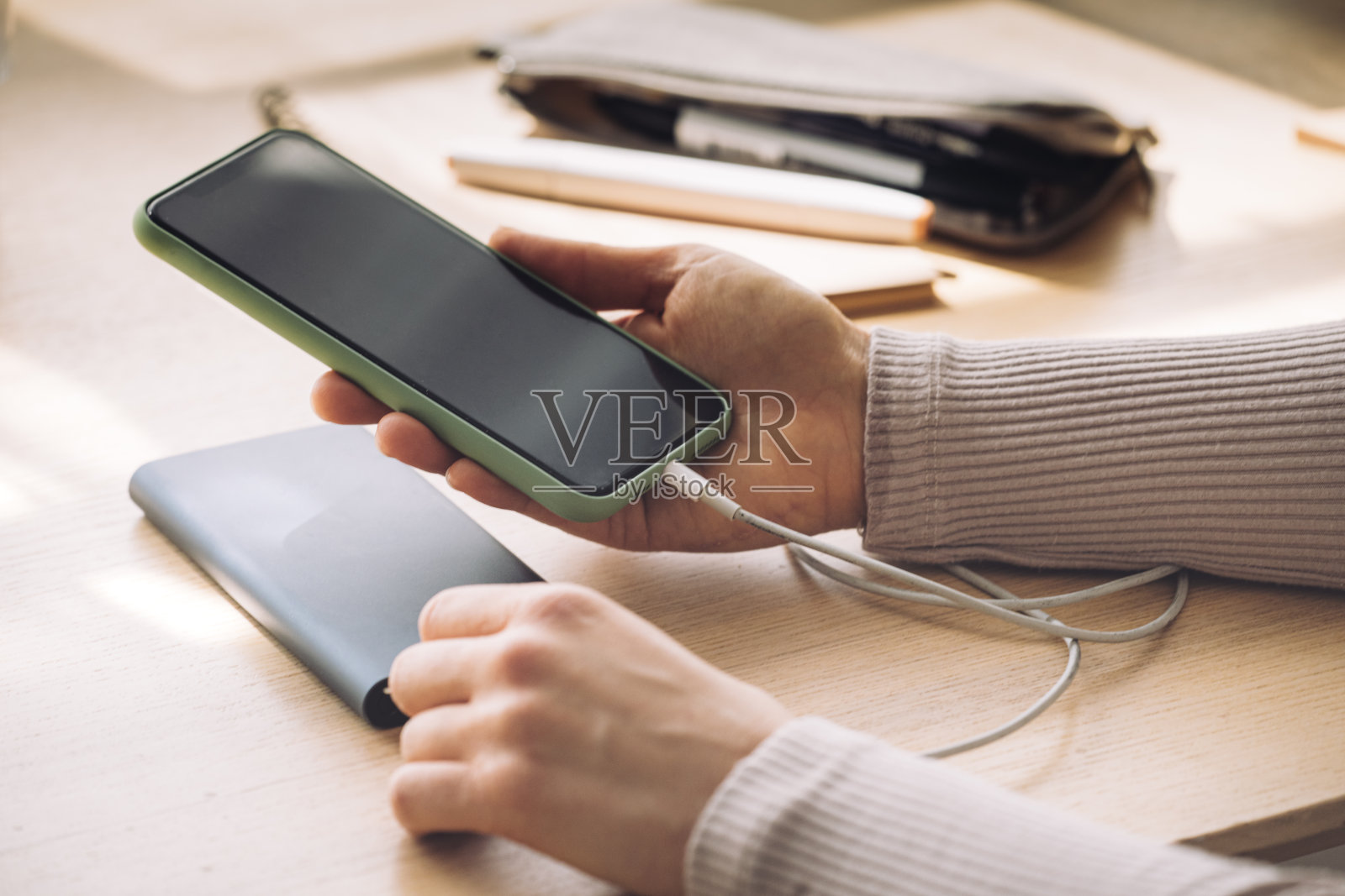 一个匿名的女人使用她的手机，而它正在充电的便携式电源银行的特写照片摄影图片