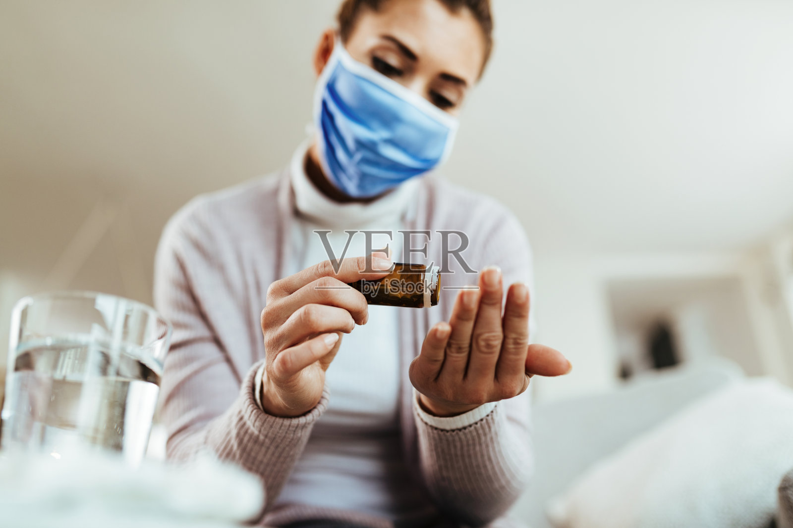 特写妇女戴口罩在家服用抗病毒药物。照片摄影图片