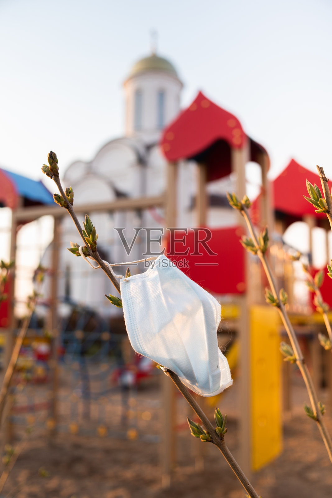 在冠状病毒和新冠肺炎大流行期间，一个医用口罩挂在基督教教堂背景的一棵树上。概念照片摄影图片