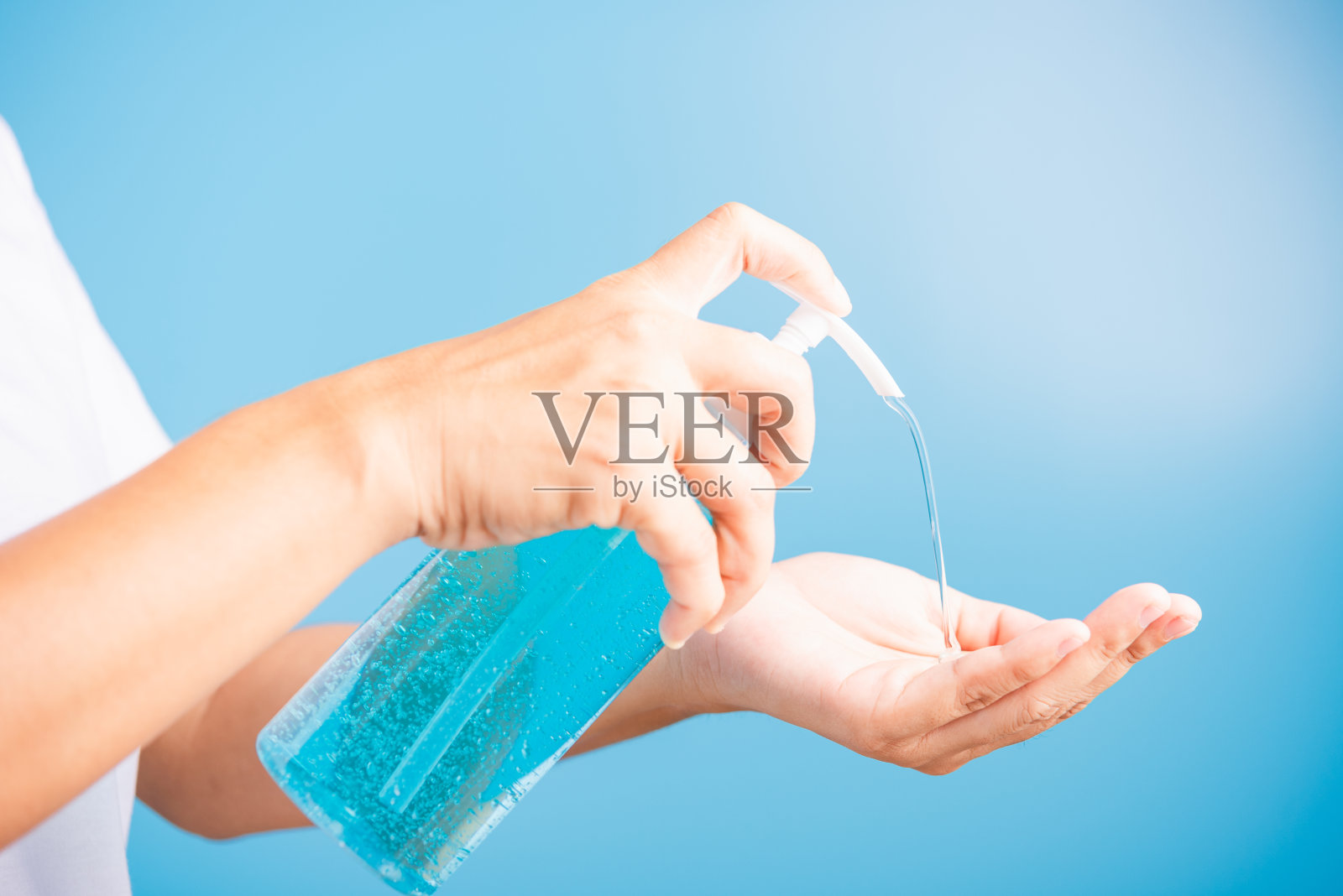 特写手亚洲年轻女性在洗手液清洁、卫生预防COVID-19或冠状病毒保护概念上使用泵式分配器消毒剂酒精凝胶，隔离在蓝色背景上照片摄影图片