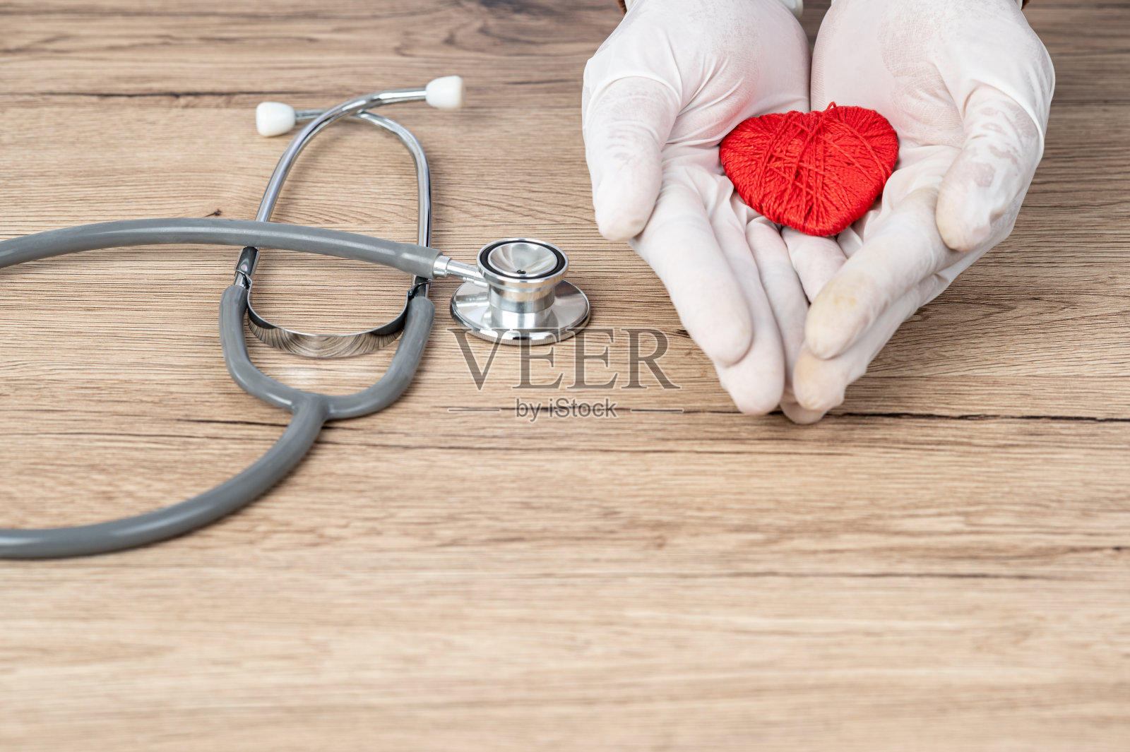 医生用手包住桌子上的红心，“心脏病概念”。照片摄影图片