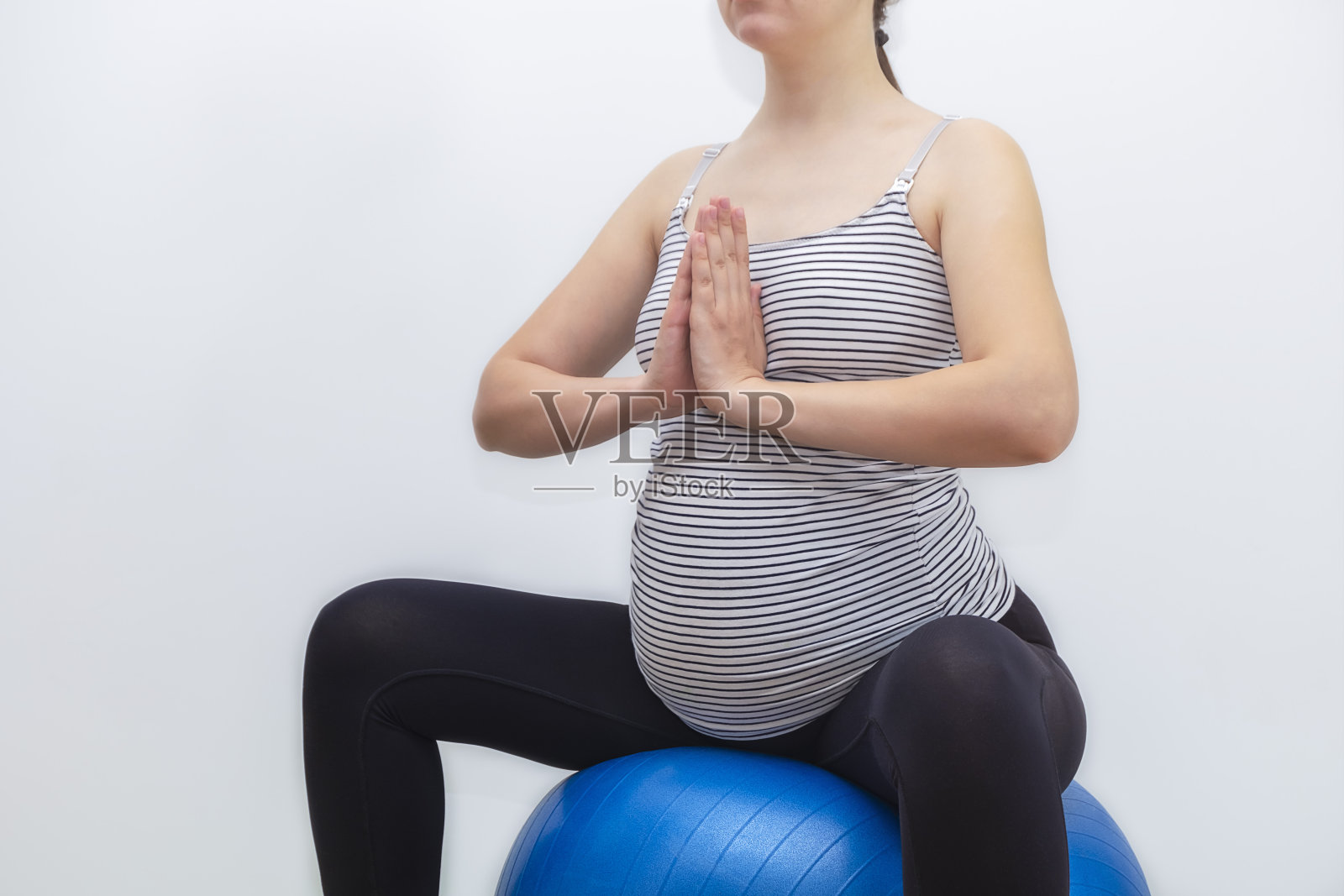 分娩球练习概念。一个不认识的孕妇坐在健身球上，白色的中性背景和文字空间照片摄影图片