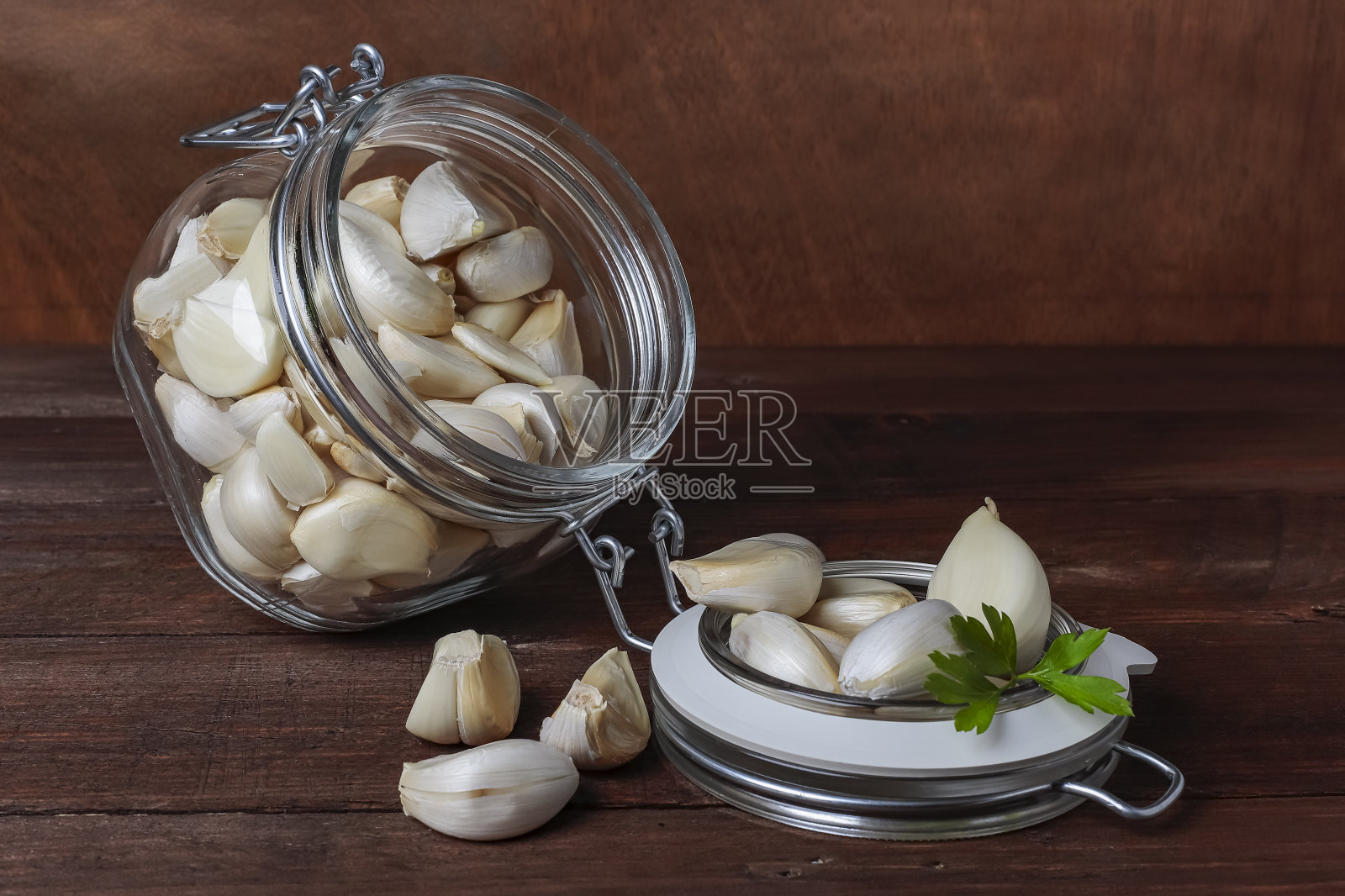 玻璃密封罐，放着蒜瓣和欧芹放在桌子上，背景是木头照片摄影图片