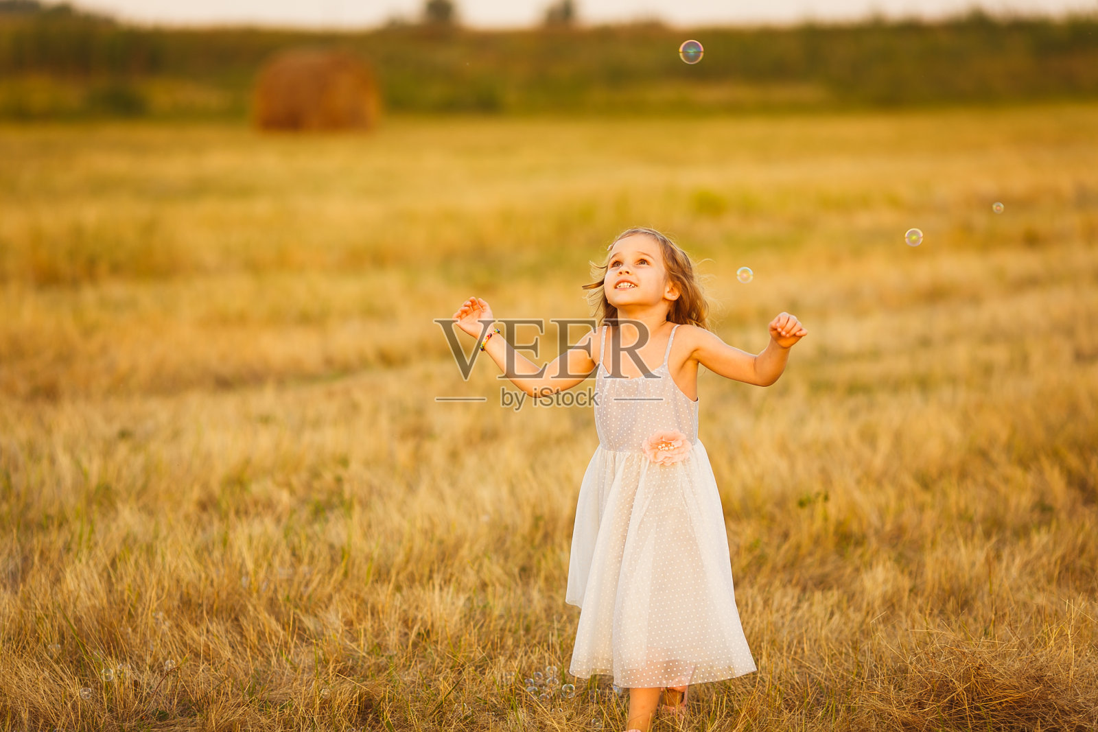 女孩追逐肥皂泡在田野日落照片摄影图片