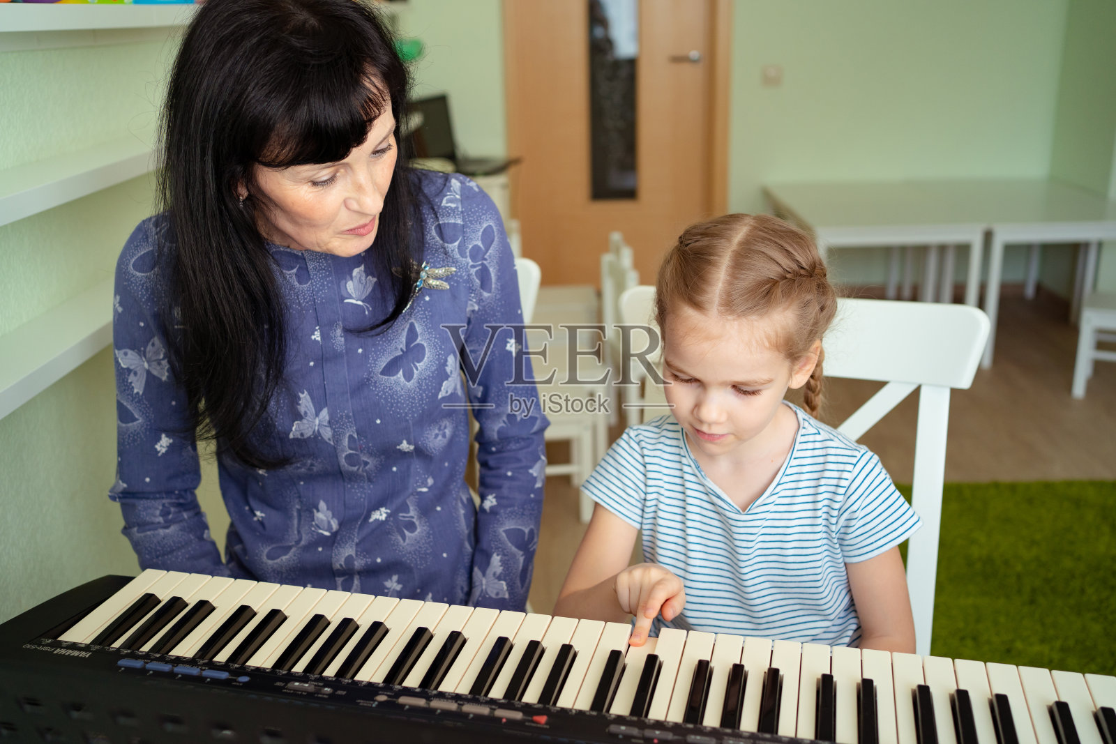 老师教小女孩玩键盘。照片摄影图片