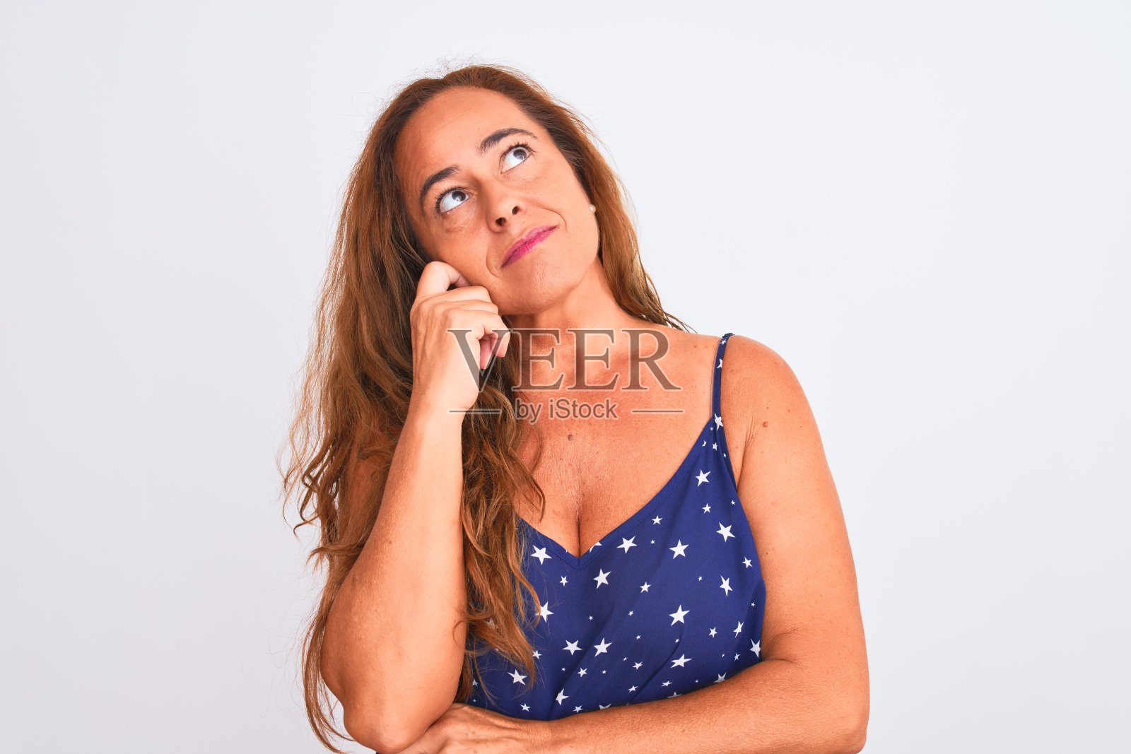中年成熟的女人站在白色孤立的背景下，手托着下巴思考问题，沉思的表情。带着沉思的微笑。怀疑的概念。照片摄影图片