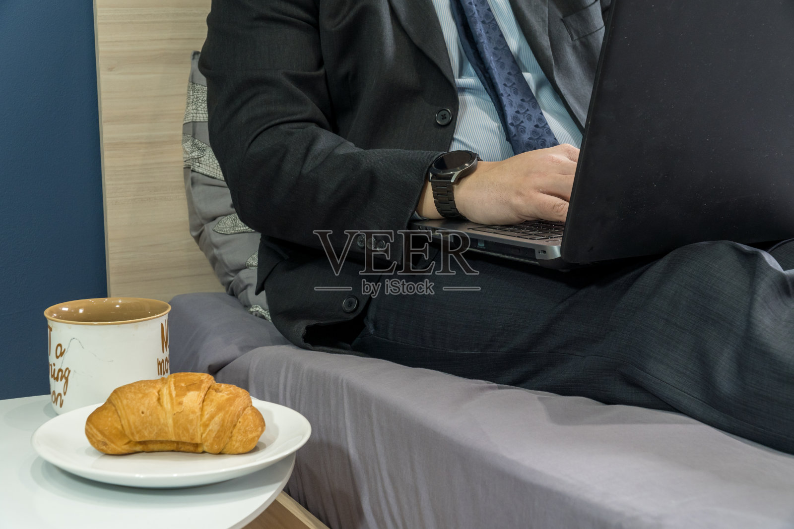 一个男人穿着西装在床上拿着笔记本电脑的家庭办公概念照片摄影图片