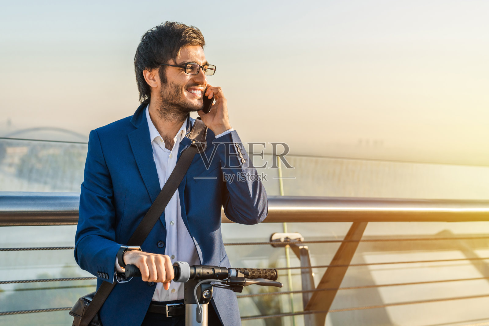 穿着西装的年轻商人骑着踏板车，在户外用手机聊天照片摄影图片