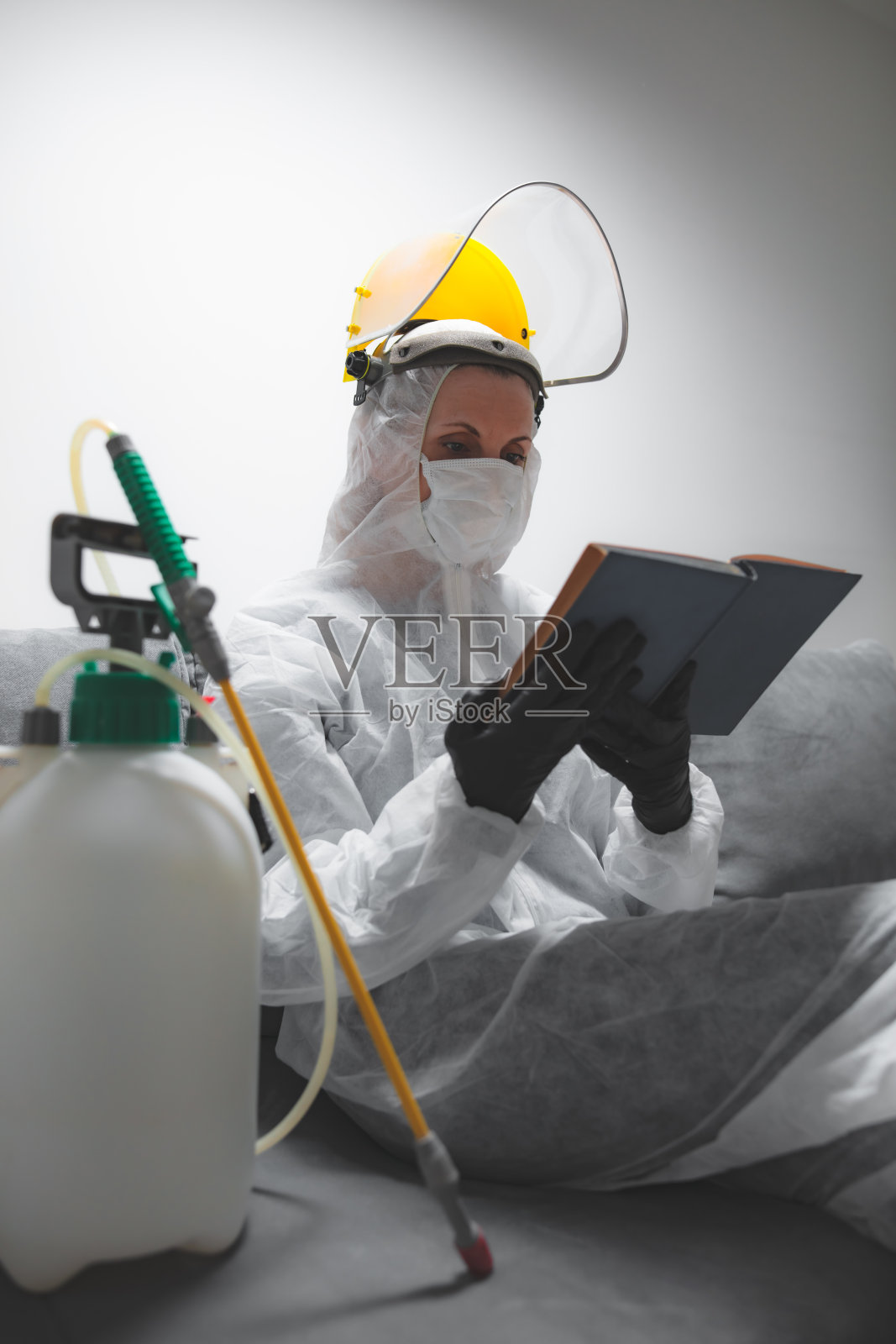 读书的人戴上防护防毒口罩、防毒服、头盔和化学去污喷雾器瓶在家隔离。照片摄影图片