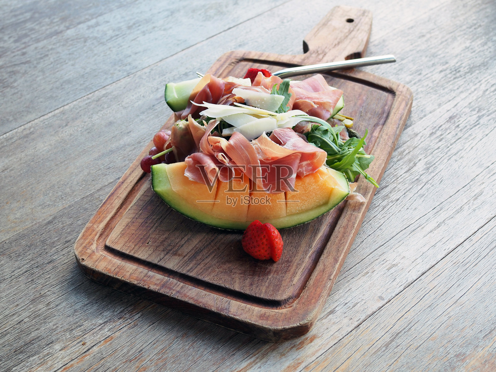 一盘帕尔玛火腿，混合蔬菜和水果，如火箭叶，新鲜草莓，甜瓜和奶酪配香醋酱。照片摄影图片