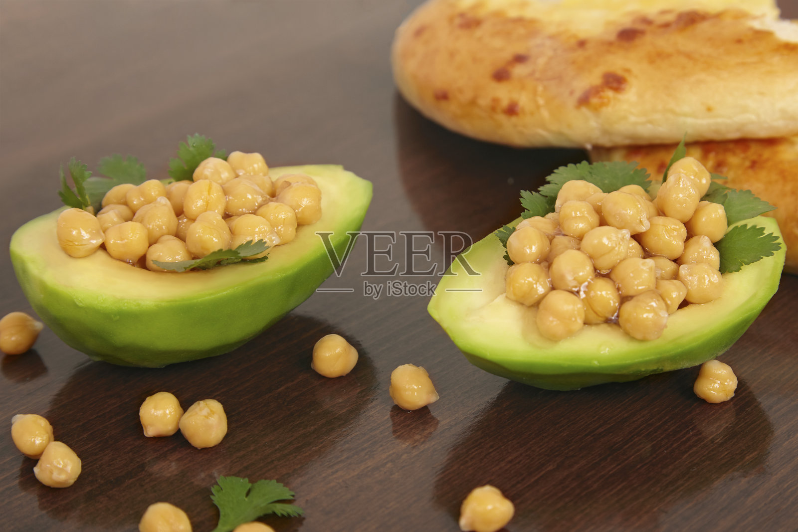 切成一半的牛油果，里面有煮鹰嘴豆和欧芹，木制背景下的素食餐。照片摄影图片