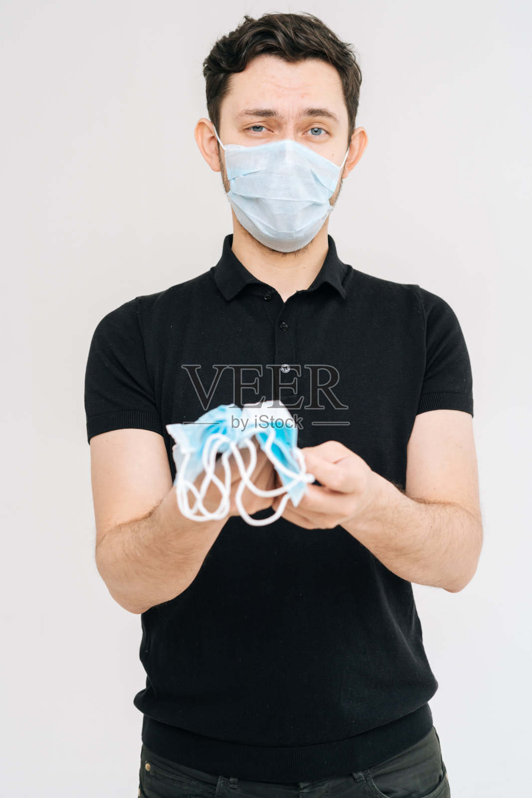 一名年轻男子戴着防护口罩，手持大量医用口罩。照片摄影图片