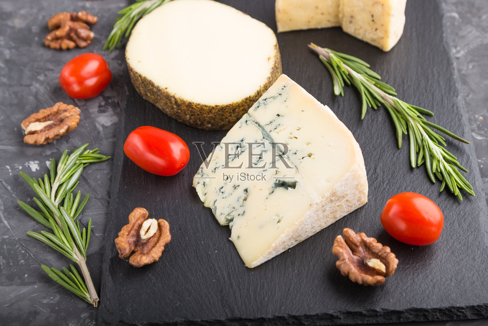 蓝色的奶酪和各种类型的奶酪，迷迭香和西红柿在黑色混凝土背景的黑色石板上。侧视图，特写，选择性聚焦。照片摄影图片